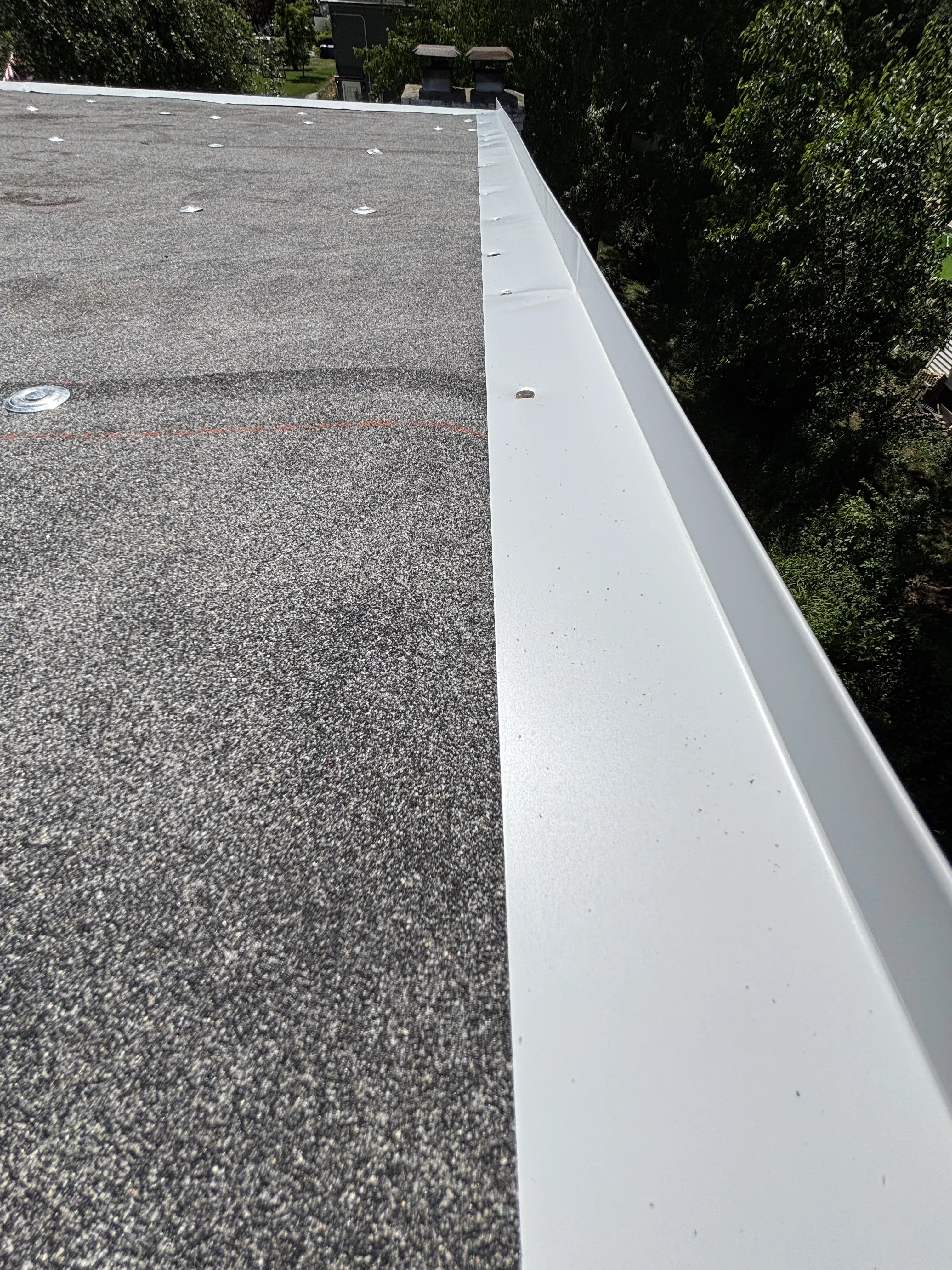 New metal capping and drip edge installed along the flat-roof perimeter where it meets the finished roof surface.