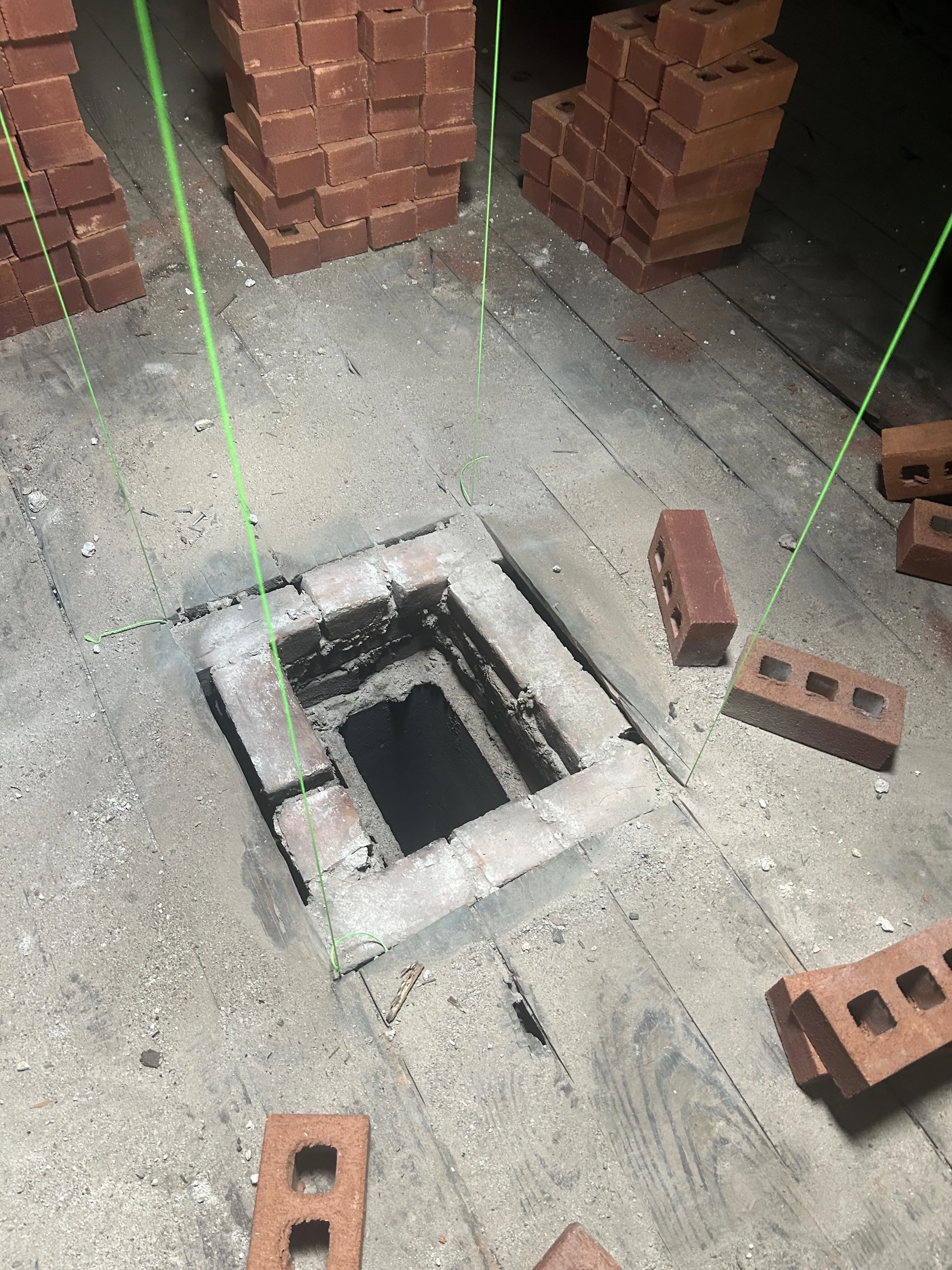 Chimney rebuild underway in the attic: the old flue opening with new bricks staged around it and laser layout lines set.