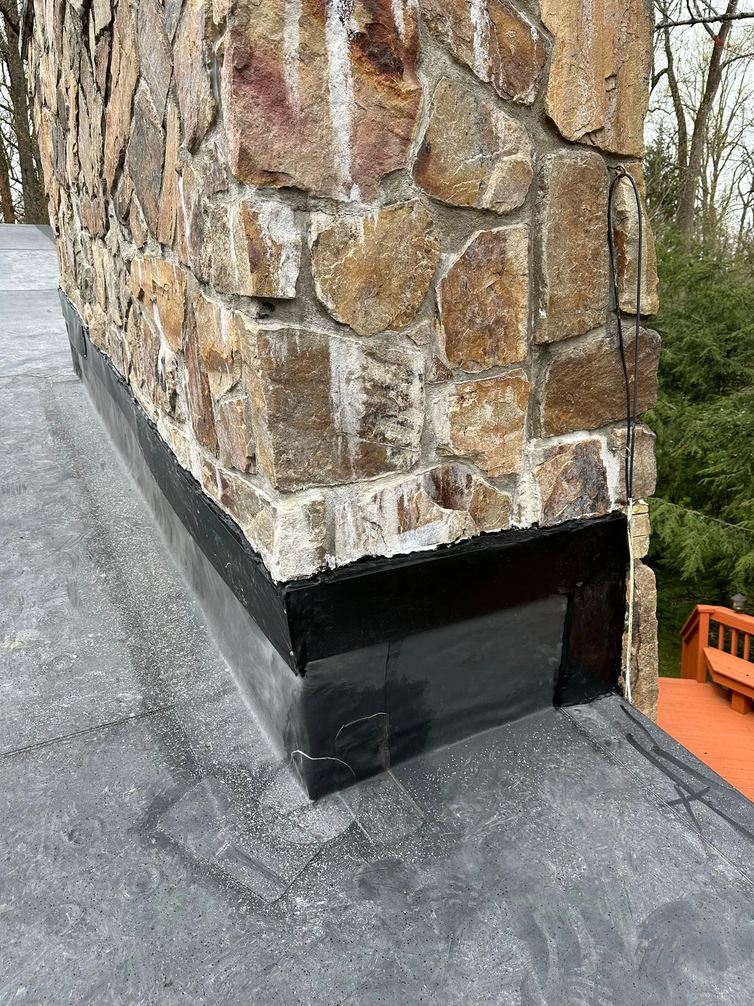 New black EPDM flashing wrapped tight around the stone chimney base on the finished flat roof.