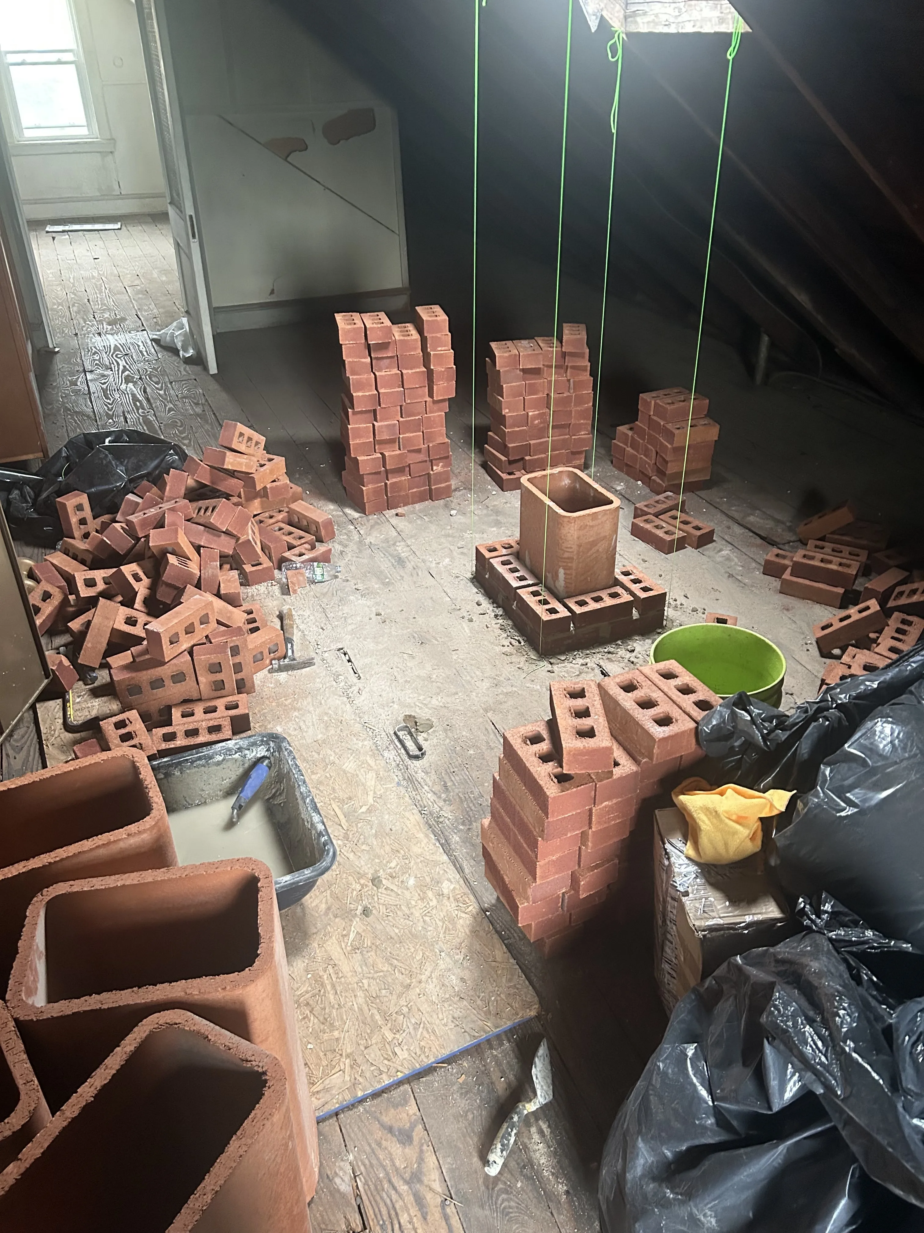 Attic staging for the chimney rebuild — new brick stacked by the bundle alongside clay flue-liner tiles.