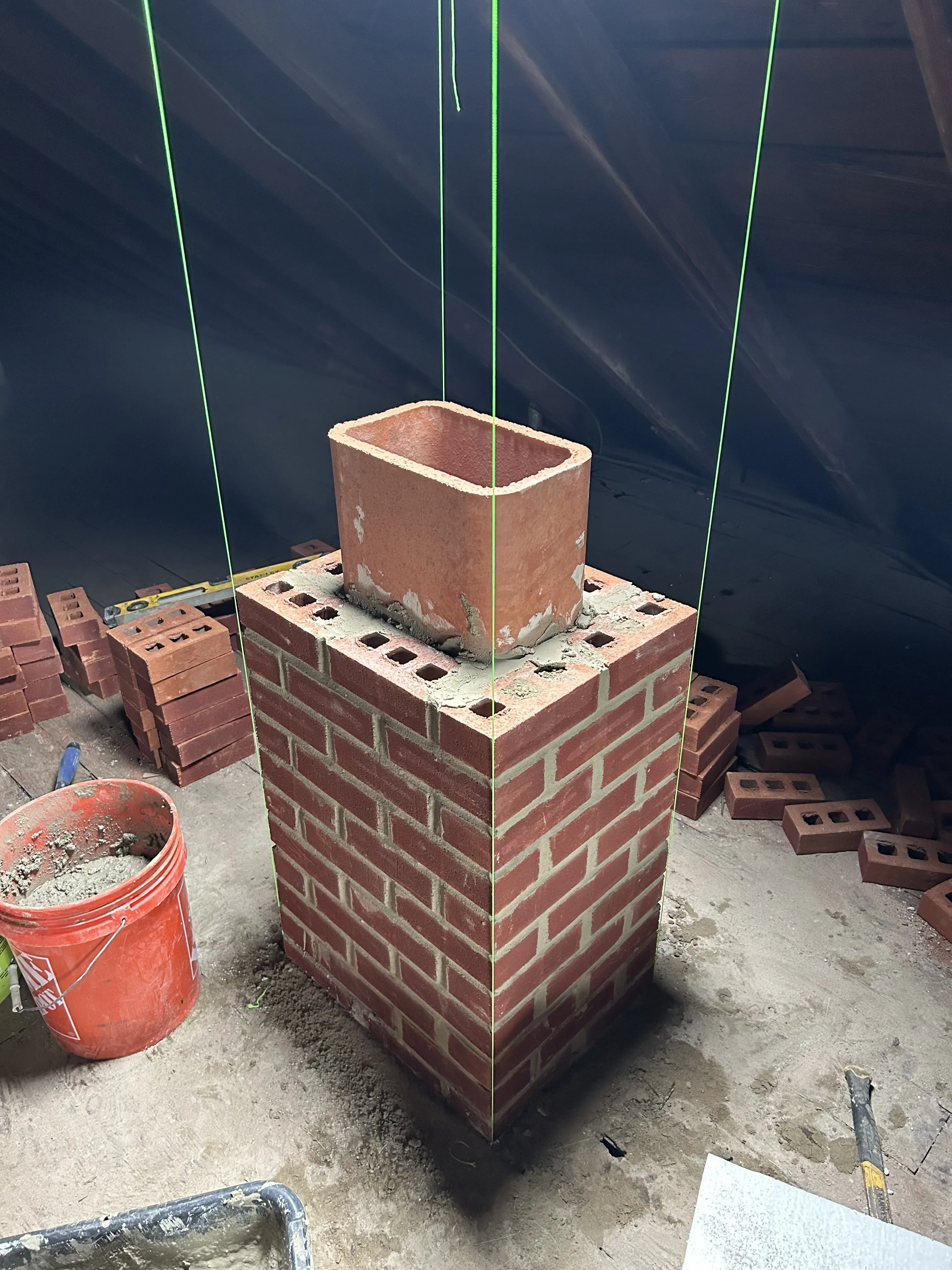 New brick chimney being laid course by course in the attic around a clay flue liner.