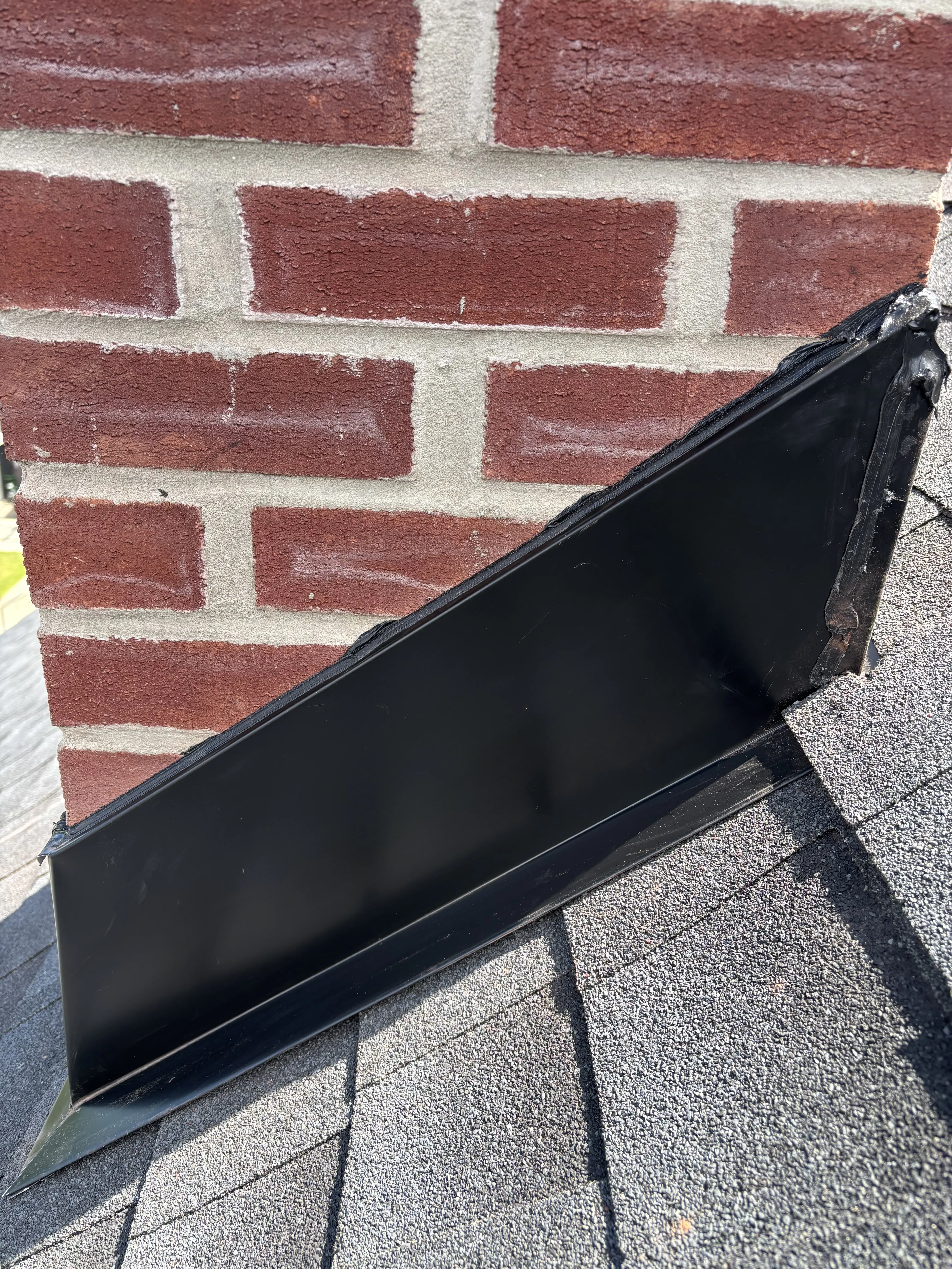 New black metal counter-flashing fitted where the chimney meets the shingles to keep water out of the joint.