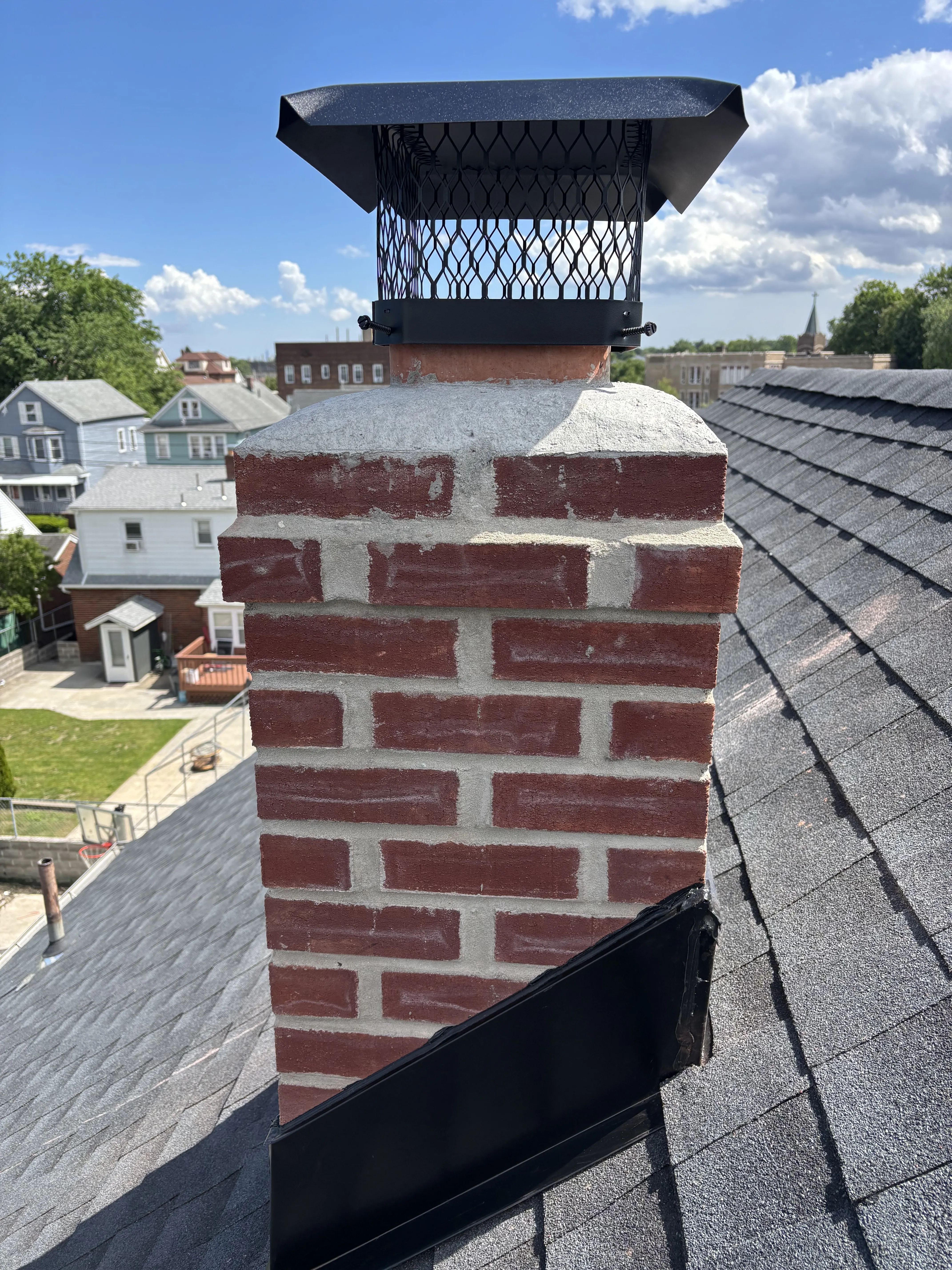 Rebuilt brick chimney with a new crown and screened cap, standing over the finished charcoal shingle roof.