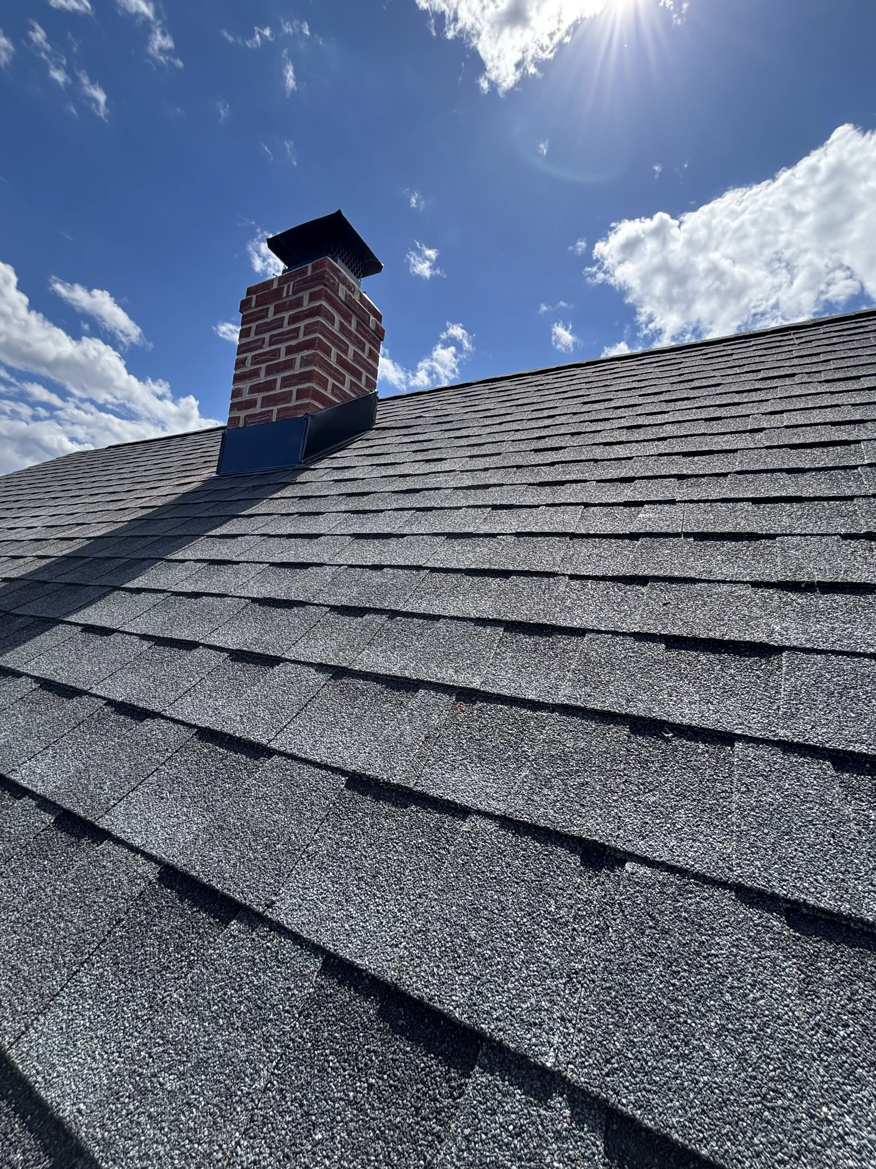 Rebuilt brick chimney capped and flashed, viewed against the new GAF HDZ Charcoal roof and blue sky.