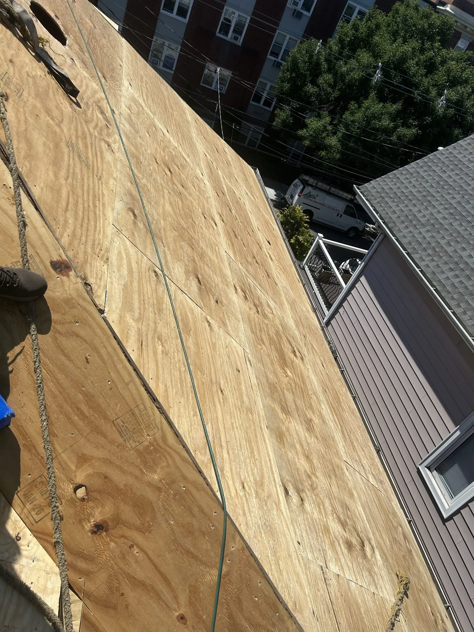 New plywood sheets laid over the original planks on the steep slope, a roofer working above.