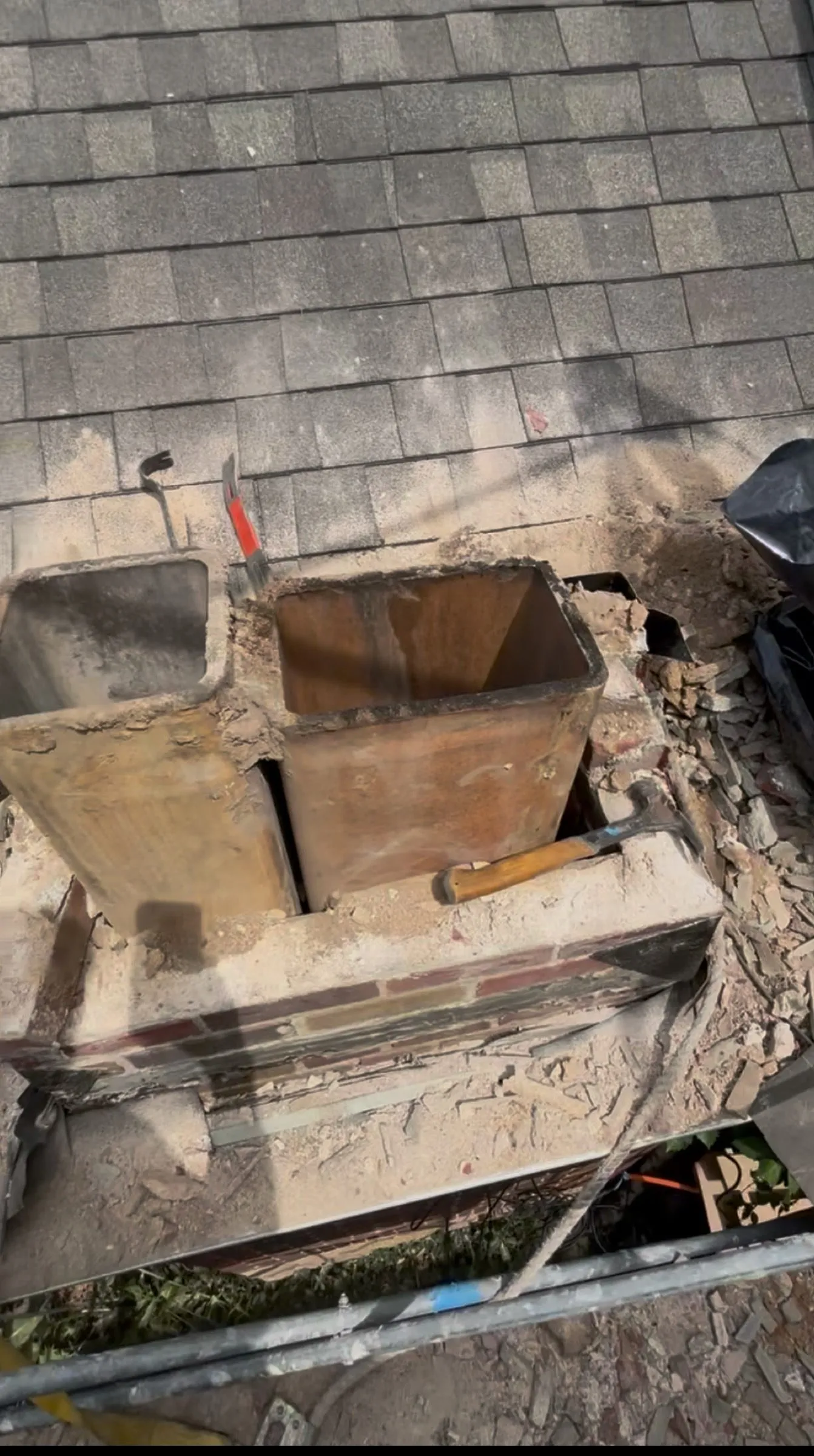 The old chimney dismantled to a stub, its cracked clay flue tiles exposed above the shingles.