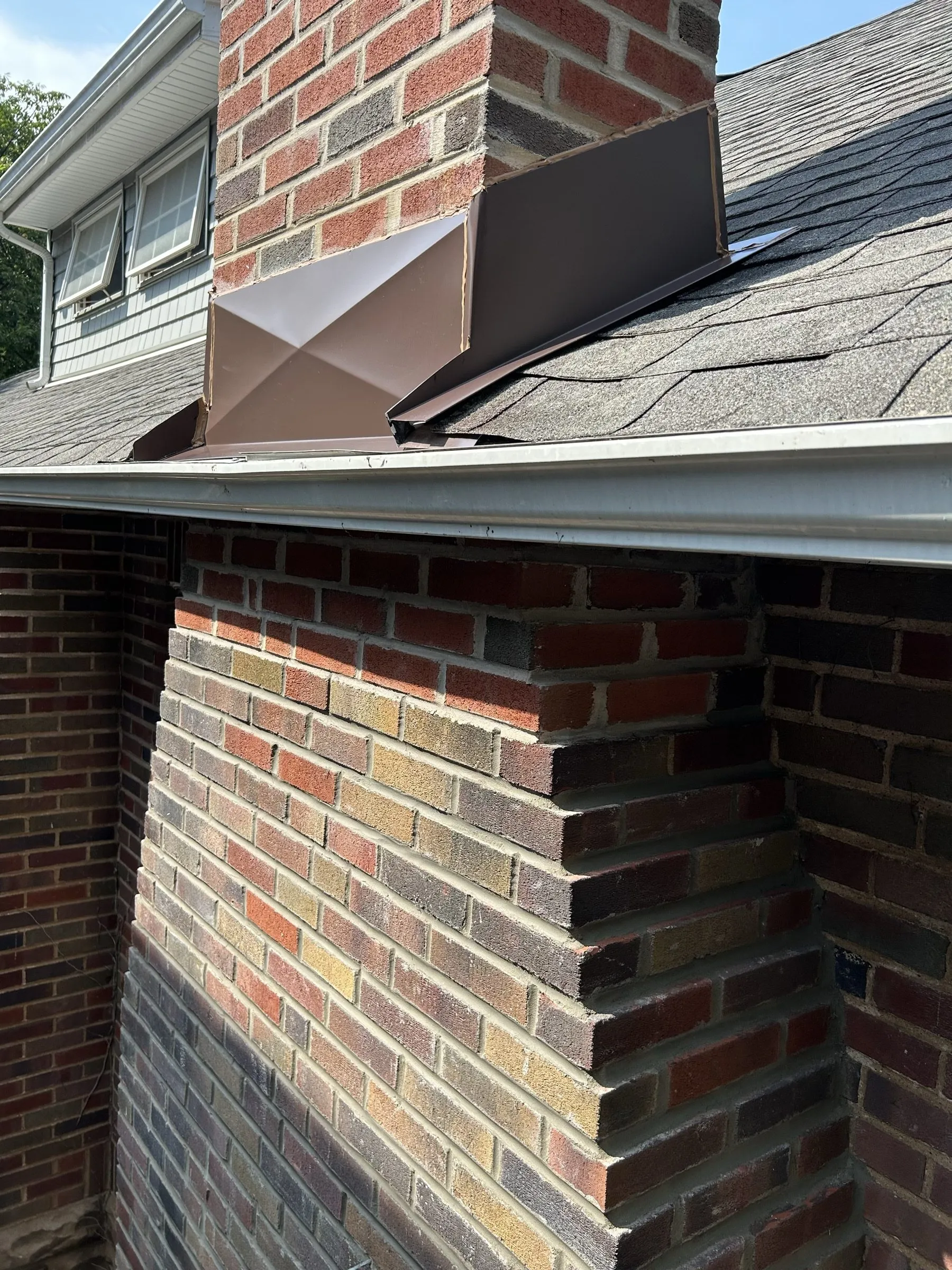 New counter flashing set into the brick where the rebuilt chimney meets the shingle roof.