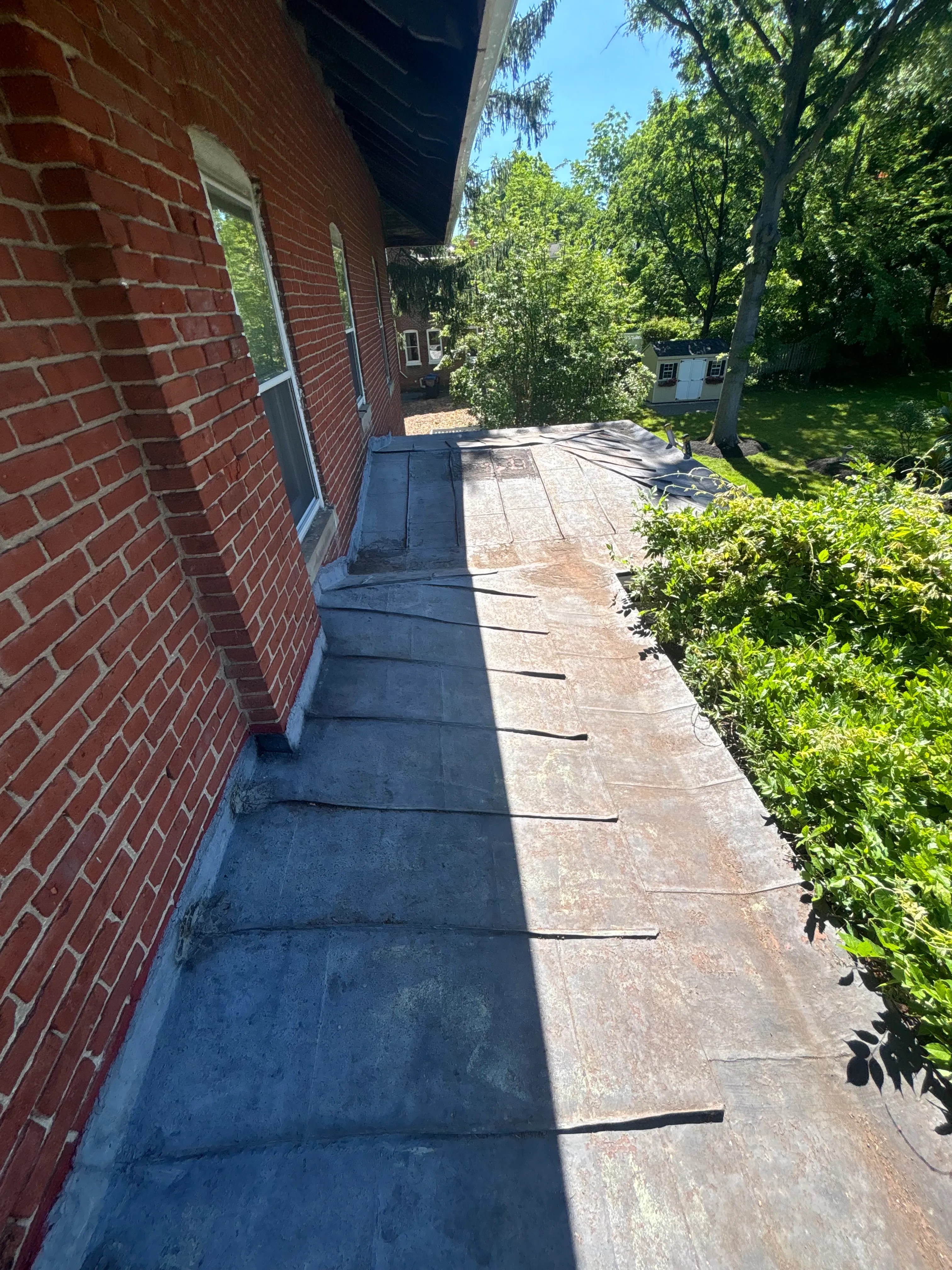 Leaking flat metal roof weathered and faded before restoration, old seams visible along the parapet.