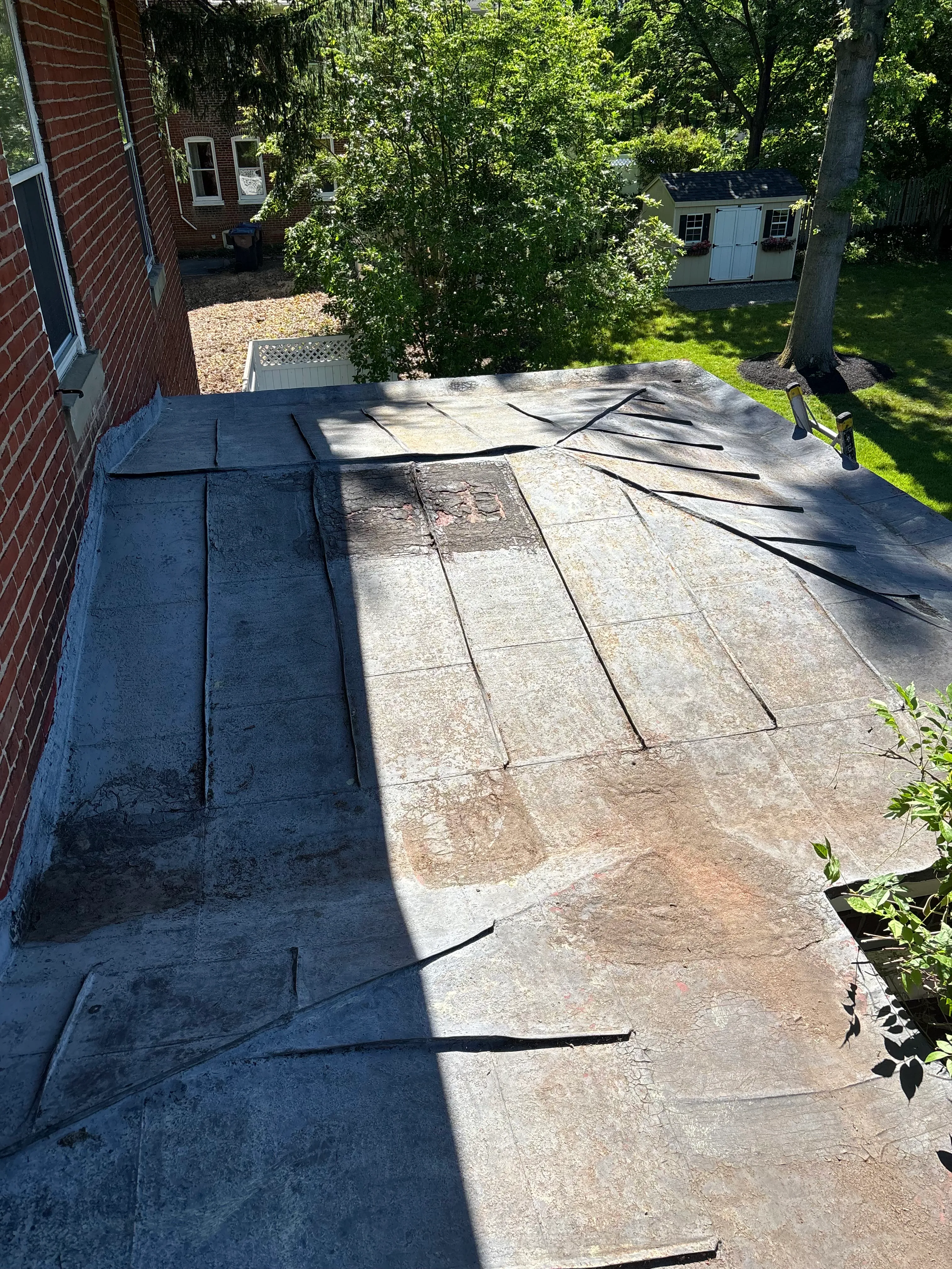 Faded, weathered roof surface with sealed vertical seams before the new coating, beside the brick wall.