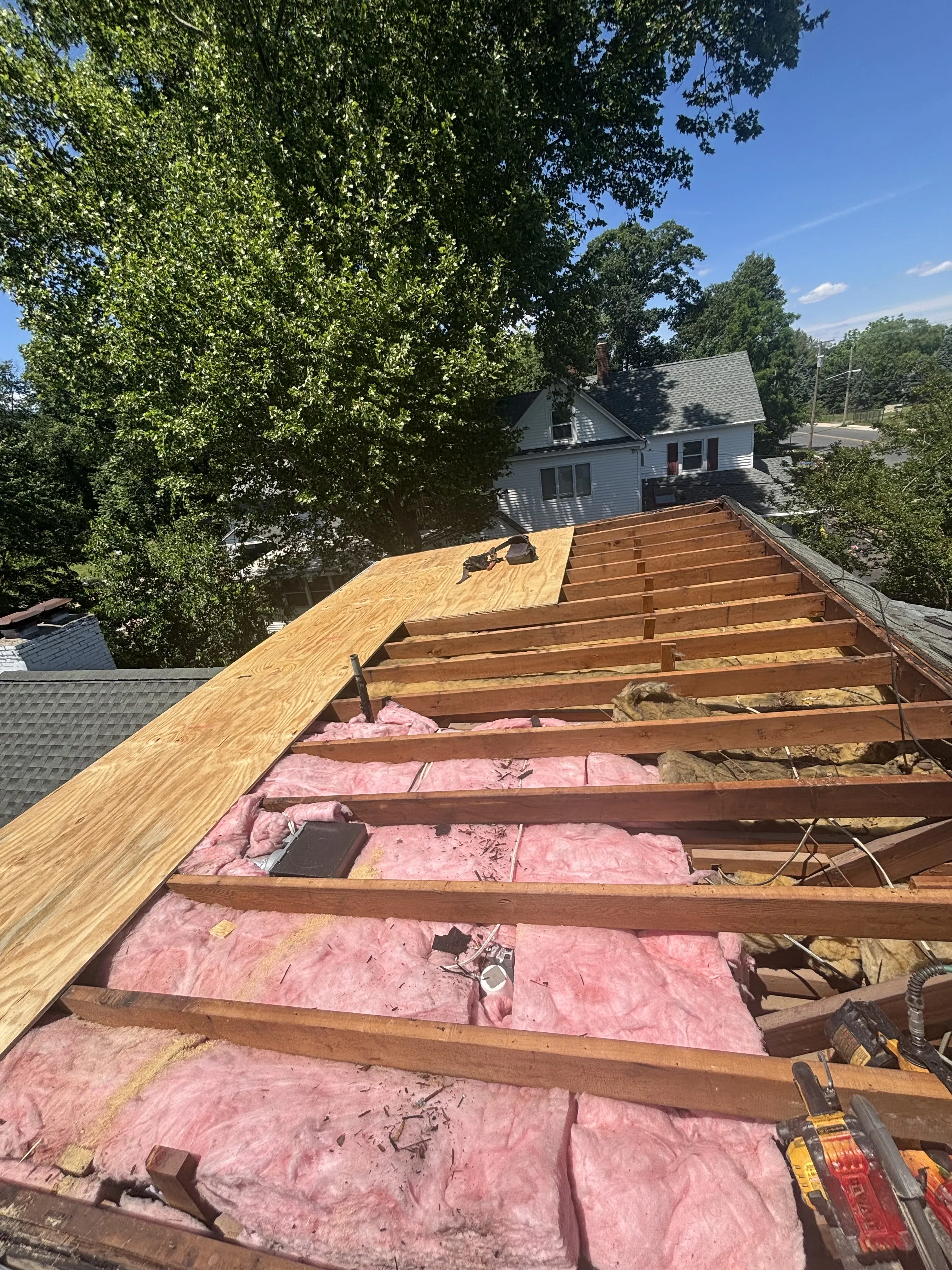 Roof opened up showing the exposed wall framing and insulation alongside new sheathing during the tear-off.