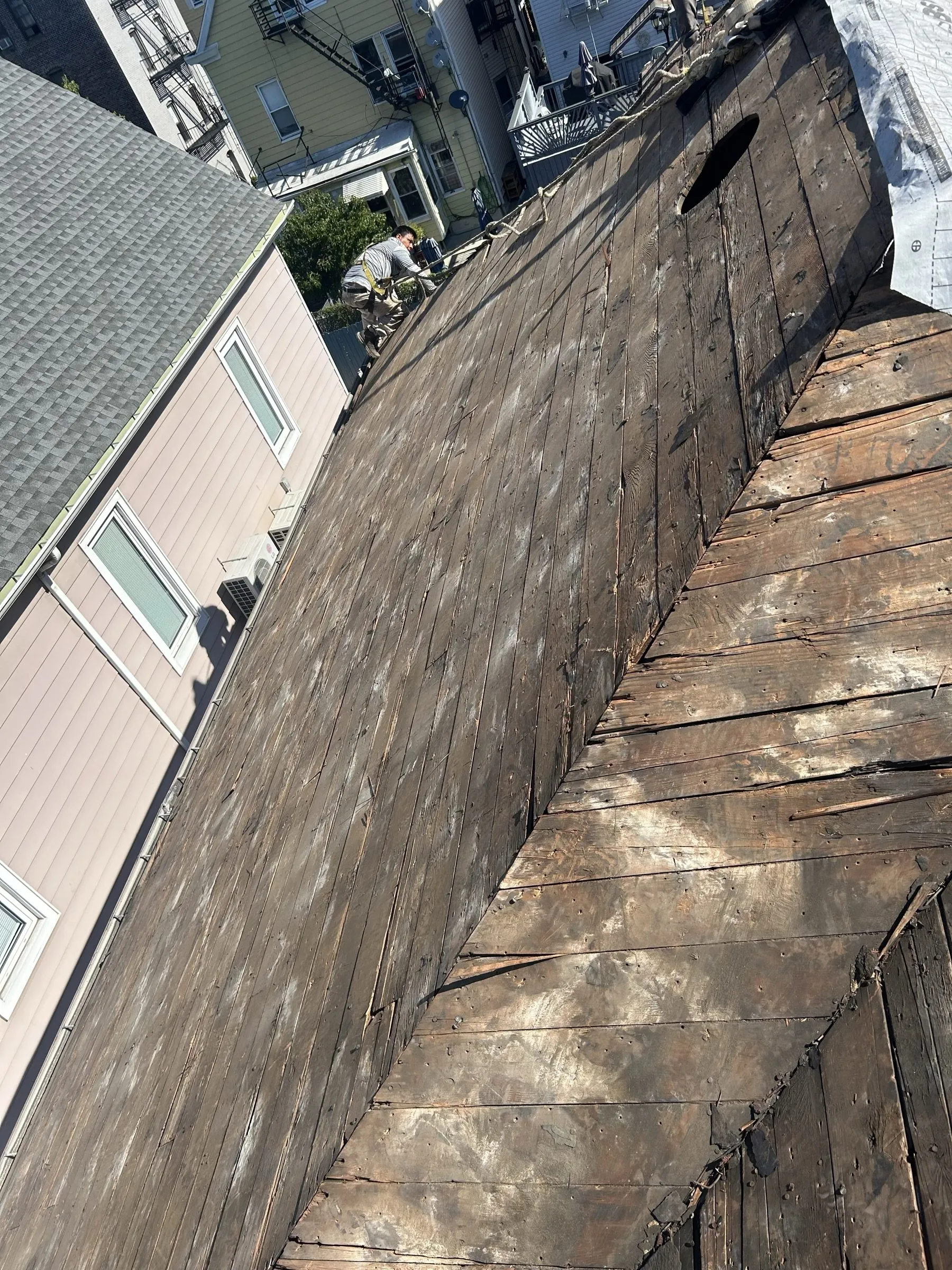 The weathered existing roof with a strip of bare plank decking opened along the slope.
