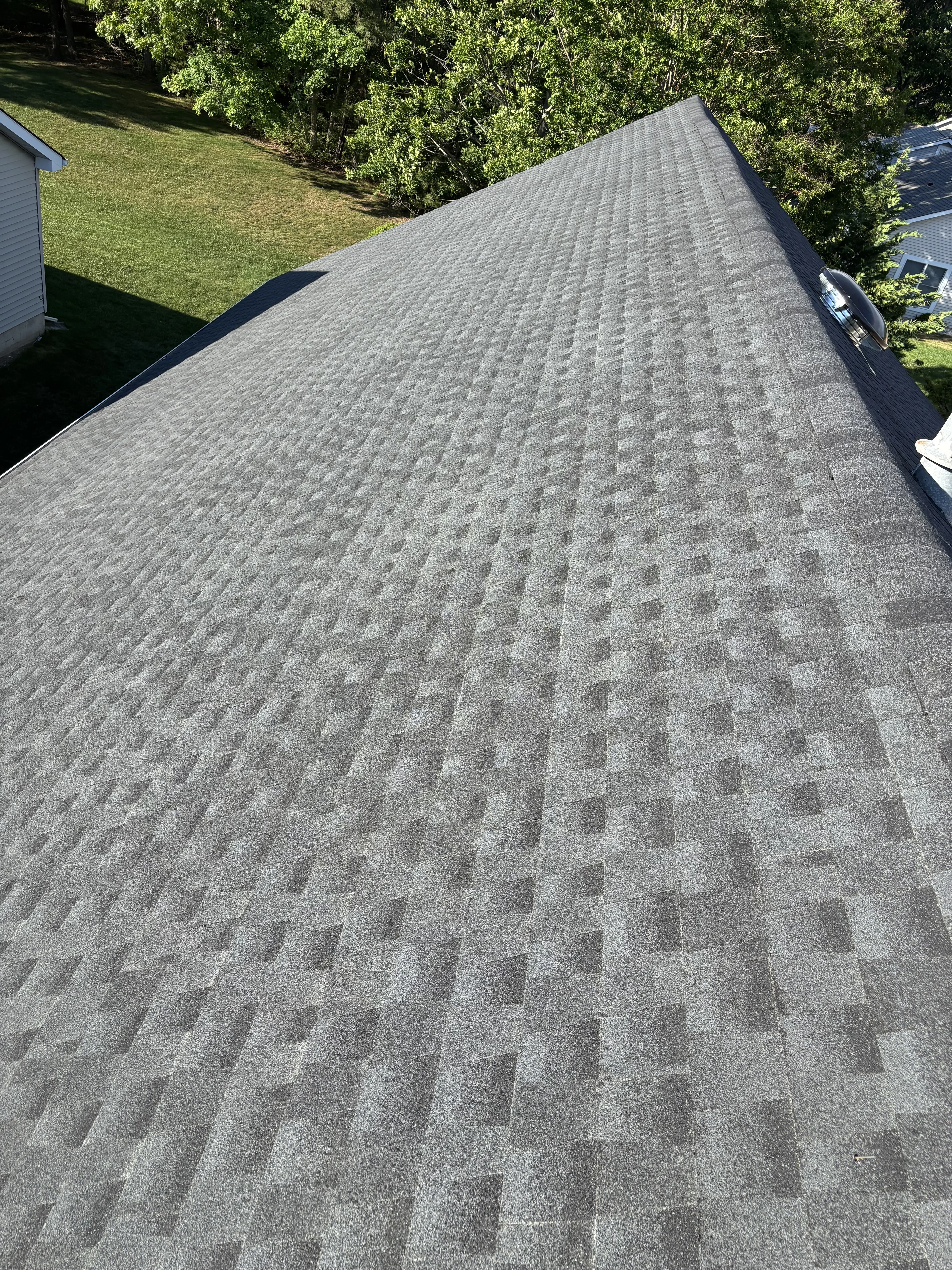 Finished shingle roof on the Toms River home, viewed across the clean new slope toward the tree line.