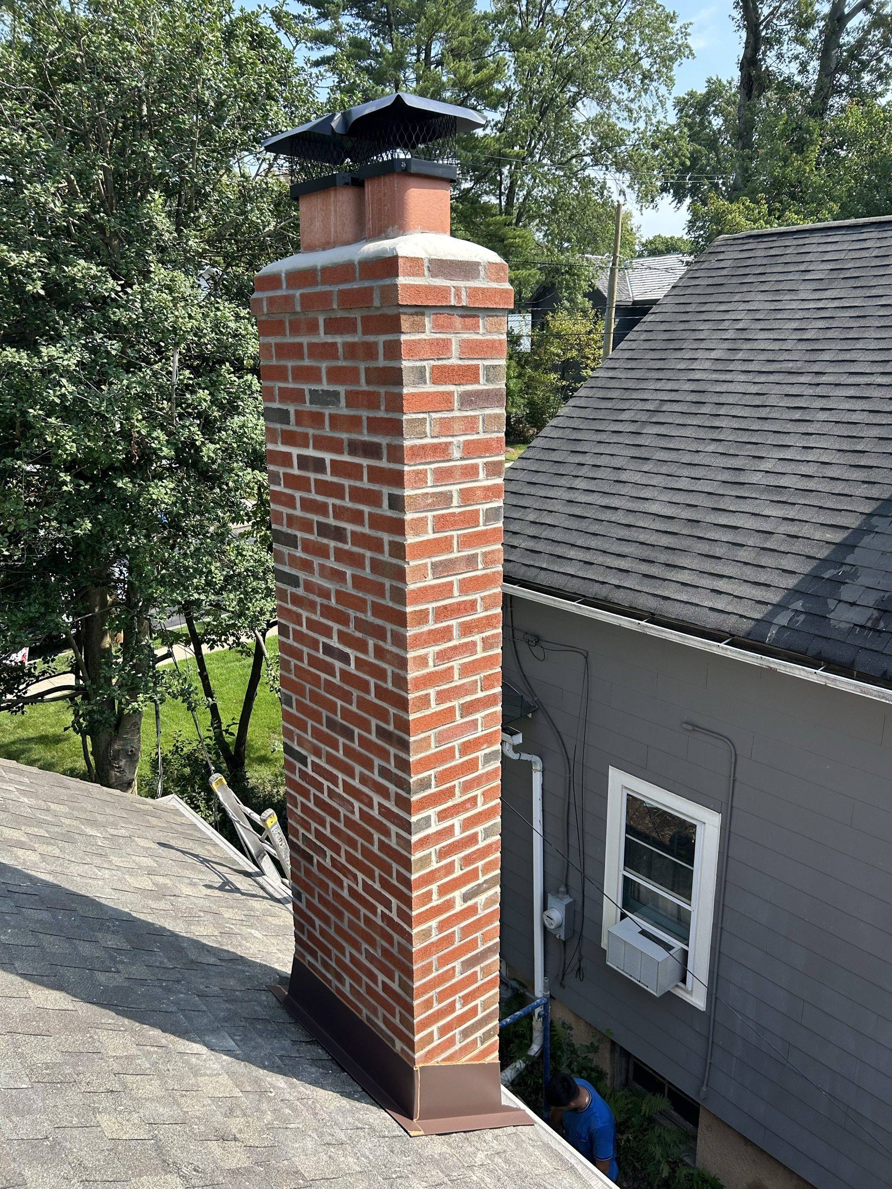 The rebuilt chimney finished in new brick with a cast crown and black cap, trees behind.