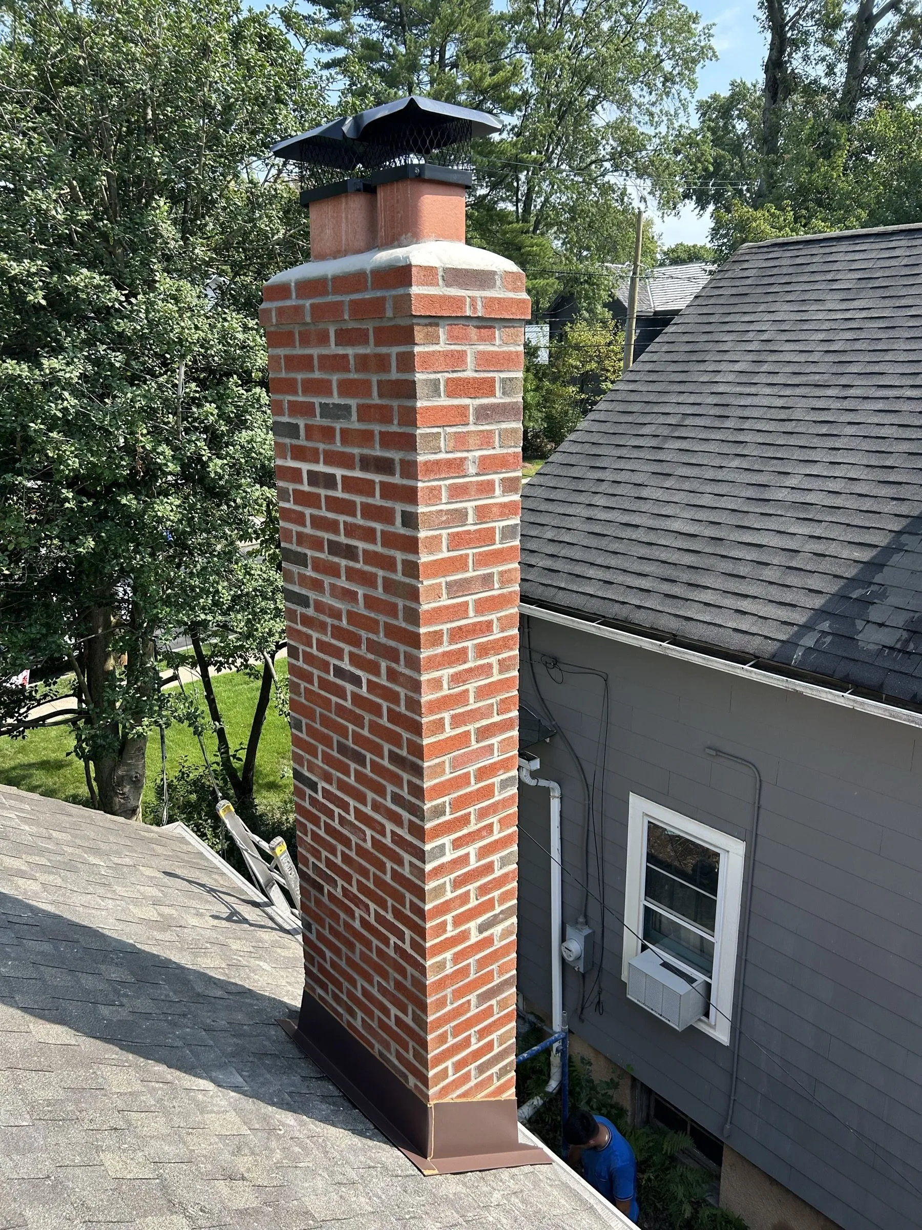 The same chimney rebuilt in new brick, running clean from the roofline up to the new cap.