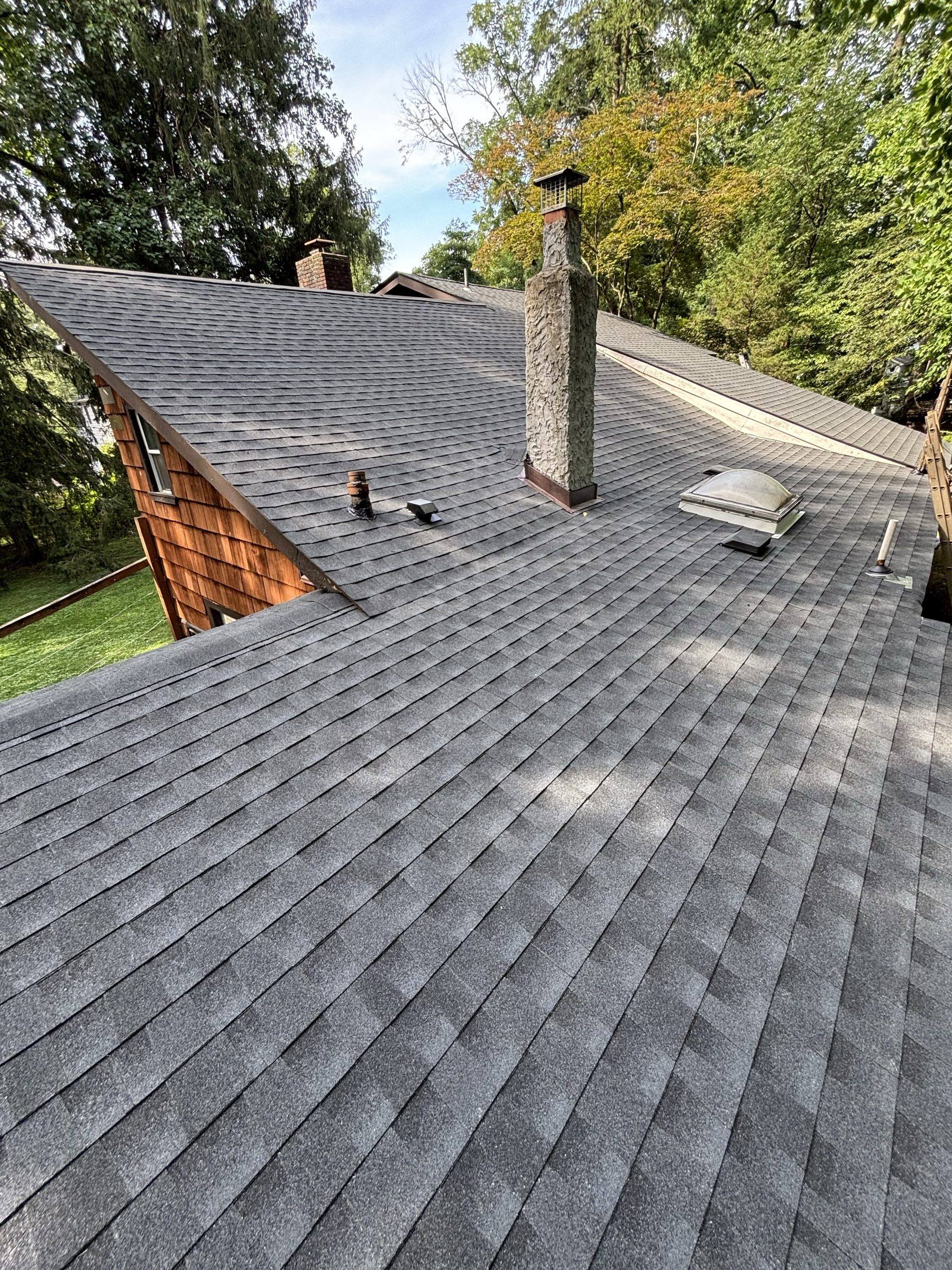 The finished roof in new shingles, vents set in, woods rising behind the house.