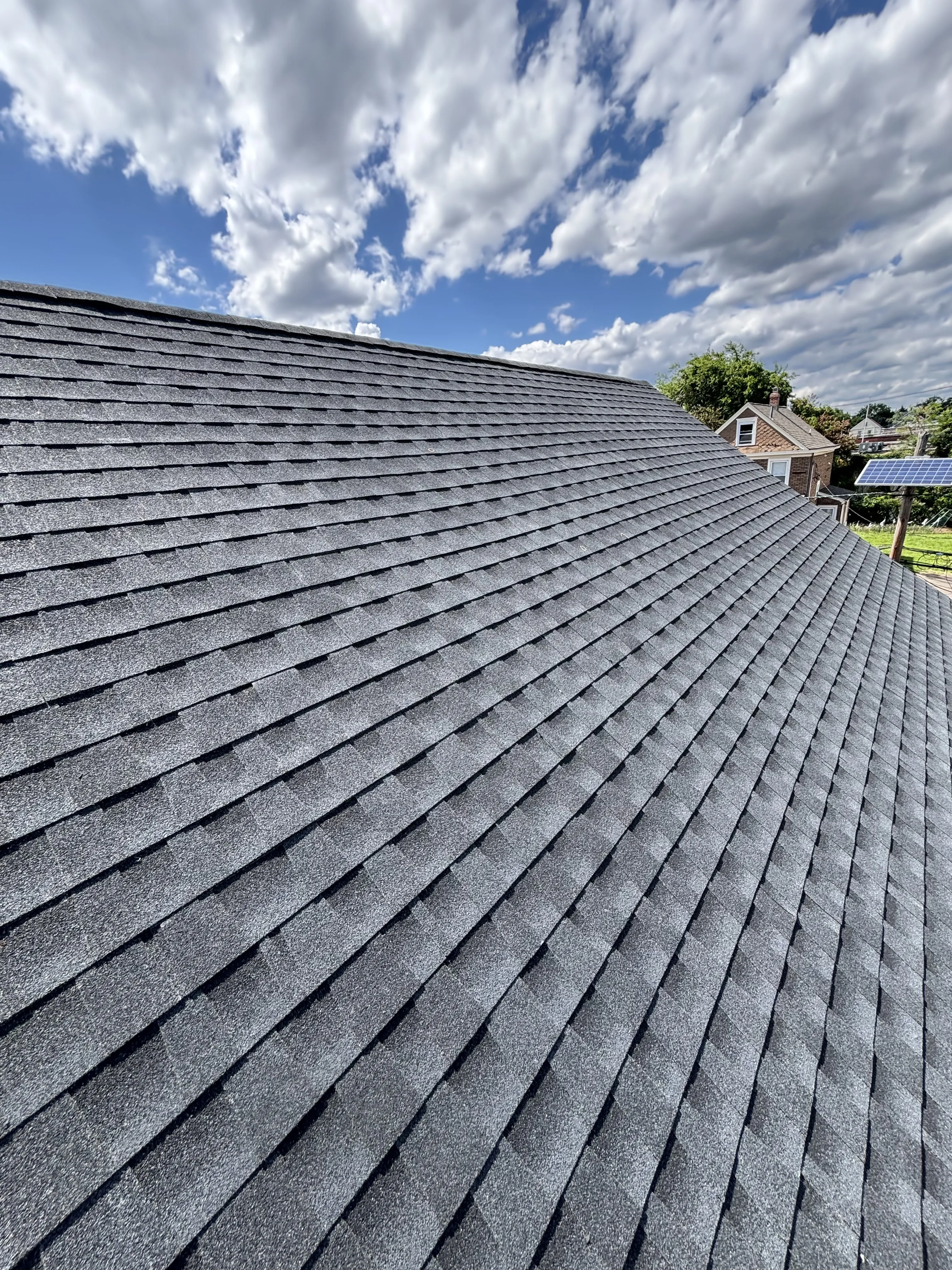 Clean rows of new GAF HDZ Charcoal architectural shingles running up the roof slope against a blue sky.