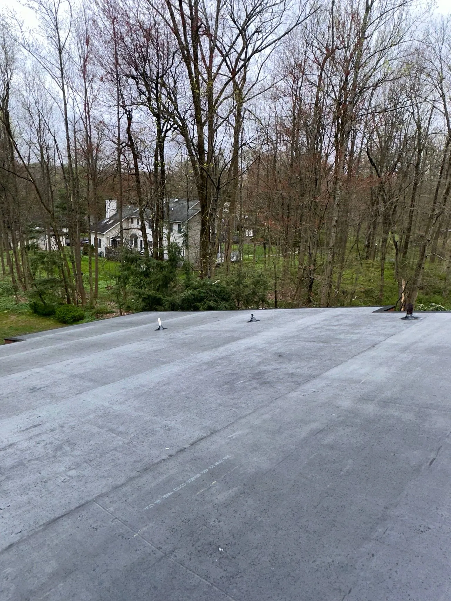 Completed EPDM flat roof with new vents, a neighboring white house through the bare trees.