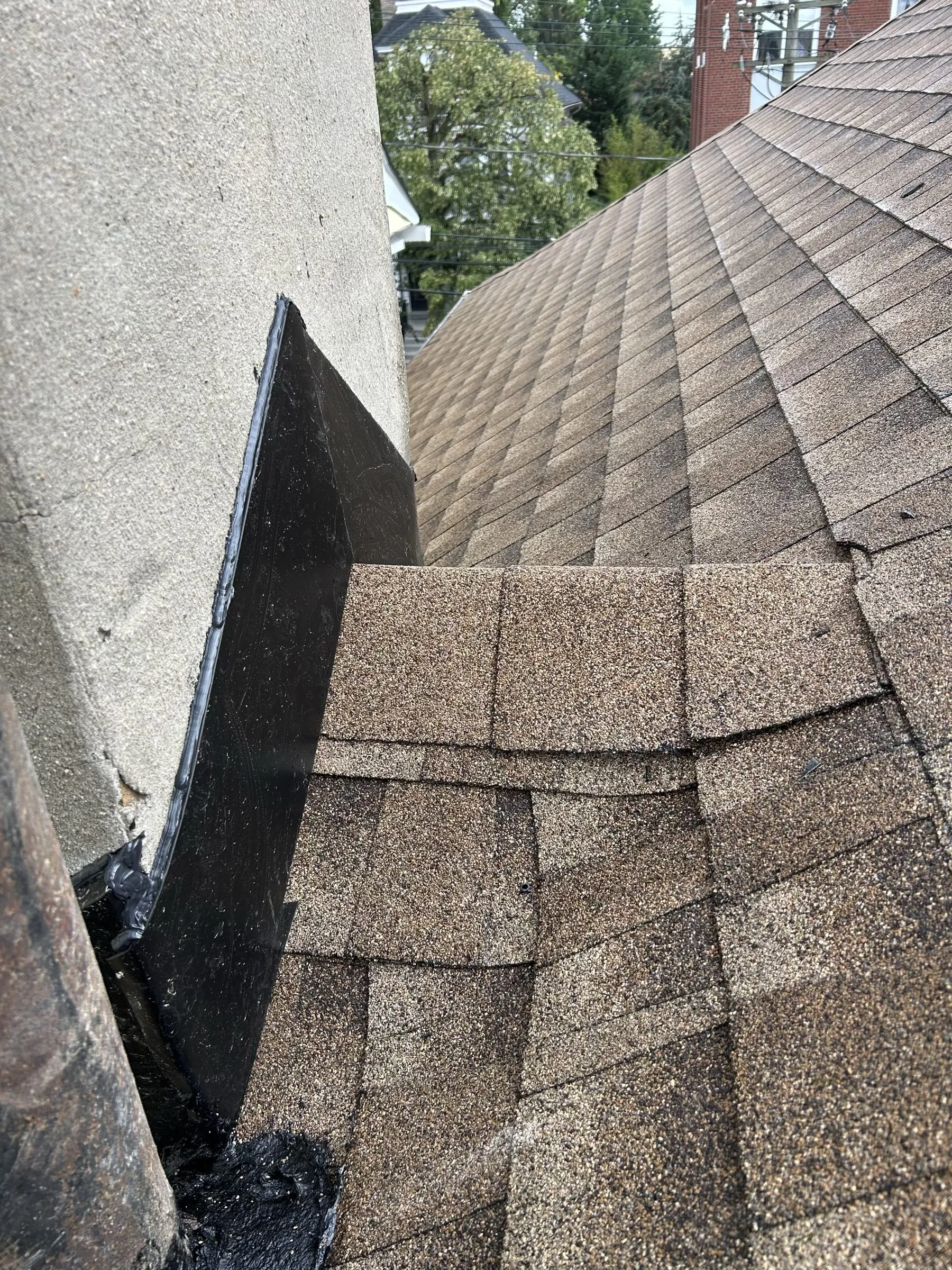 The finished slope in new shingles, dark wall flashing running up beside the chimney.