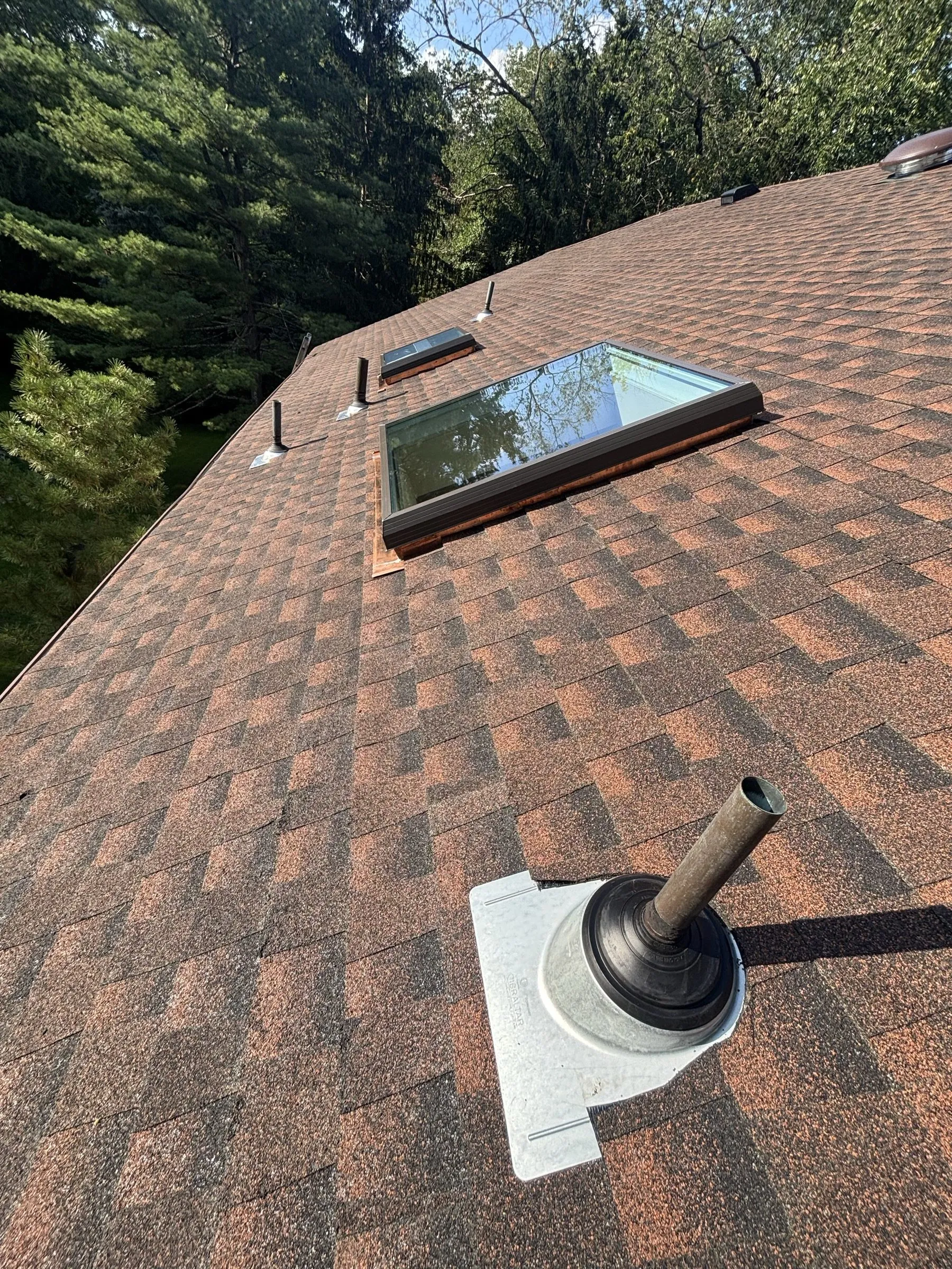 A new skylight and a flashed vent stack seated in the finished shingles.
