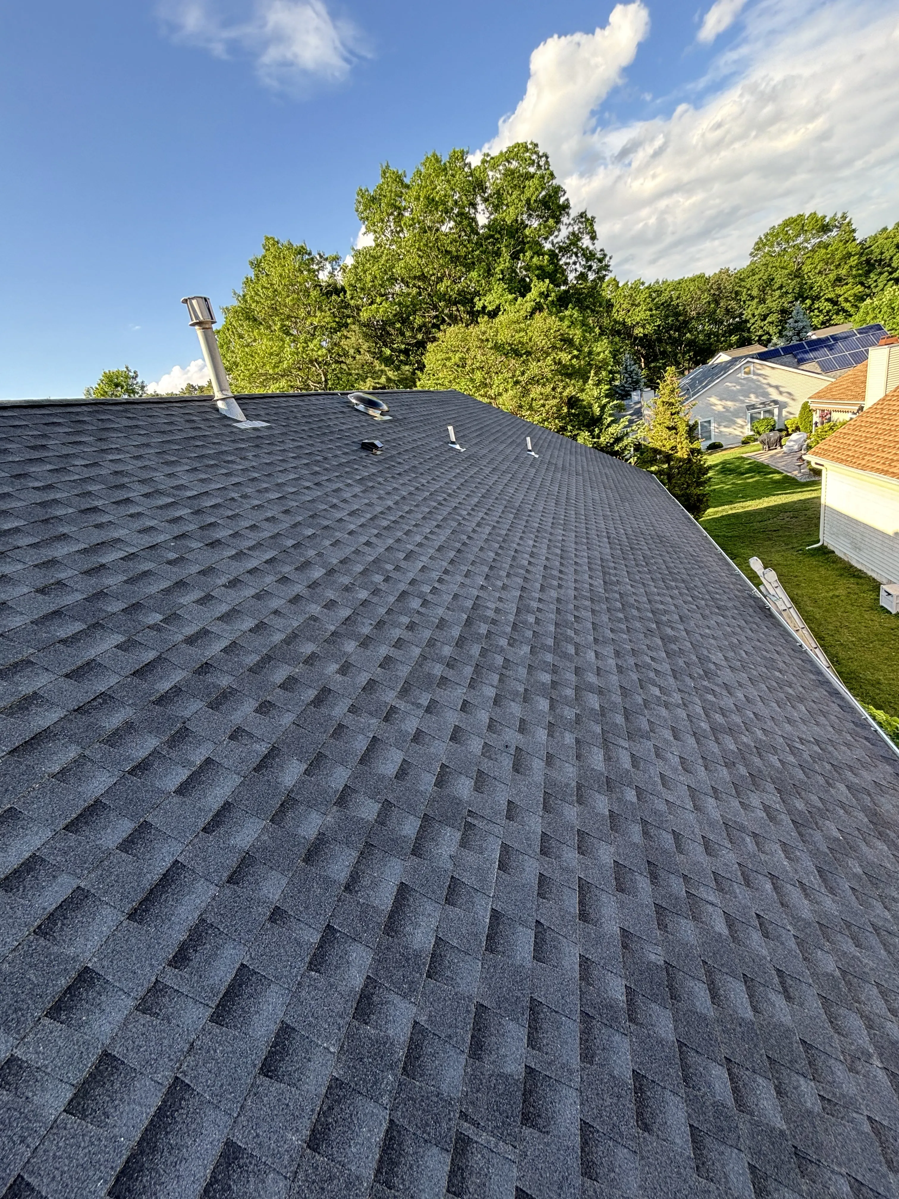 Finished shingle roof from the same elevated vantage, the new slope running down toward the home and lawn.