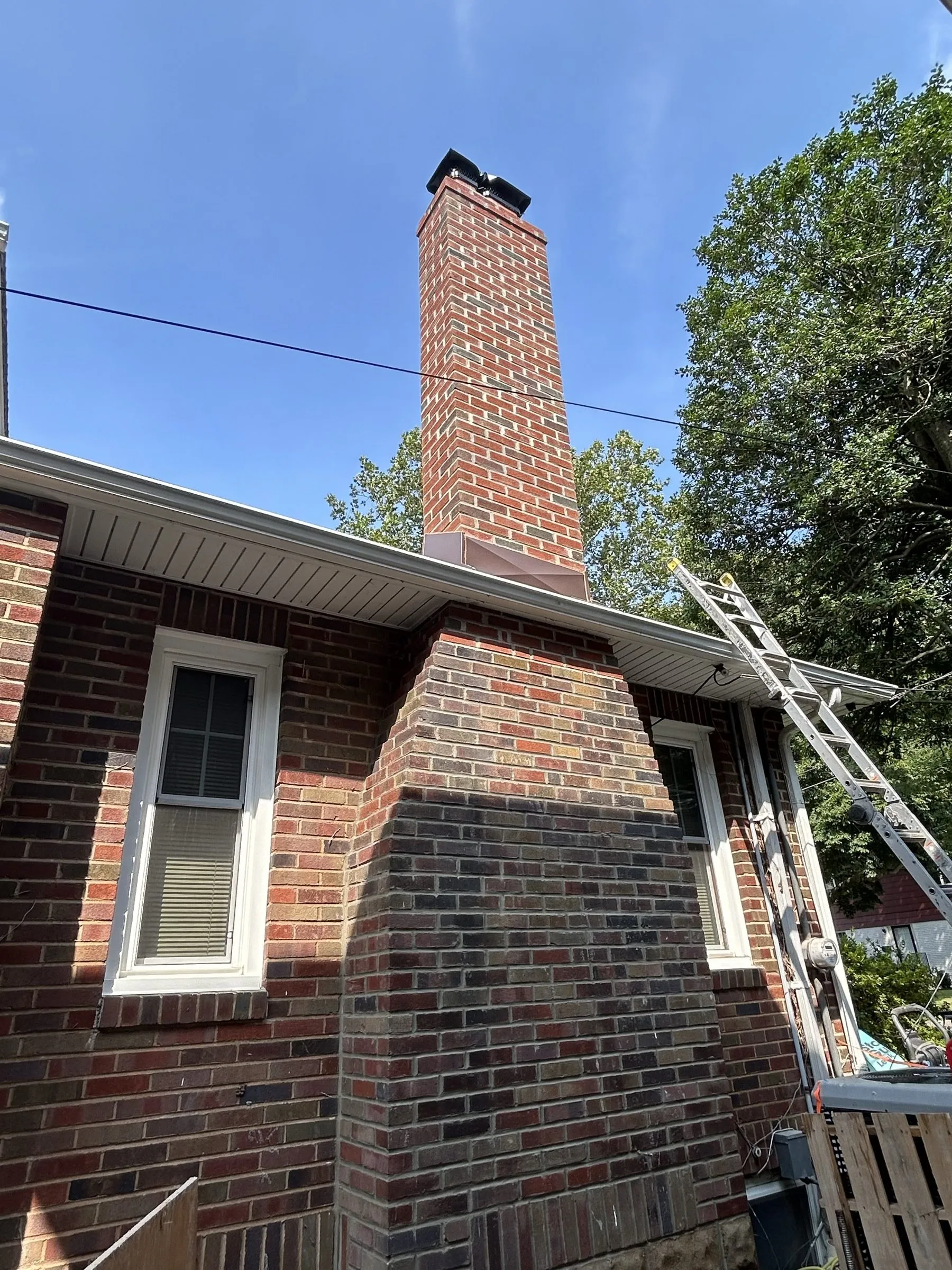 The finished chimney rising past a dormer window, seen from the driveway against blue sky.