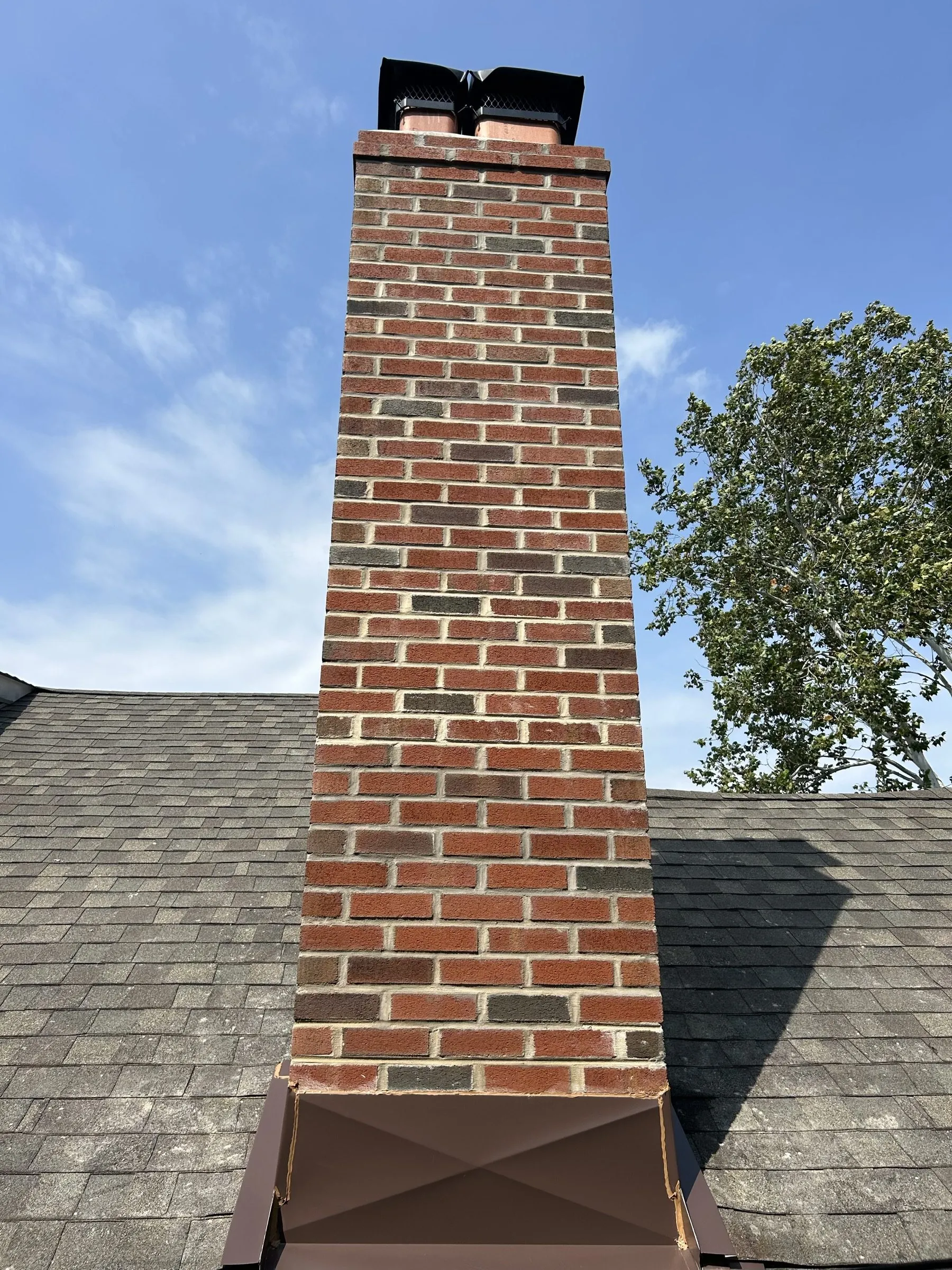 The full height of the rebuilt chimney against open sky, new brick from the roofline up.