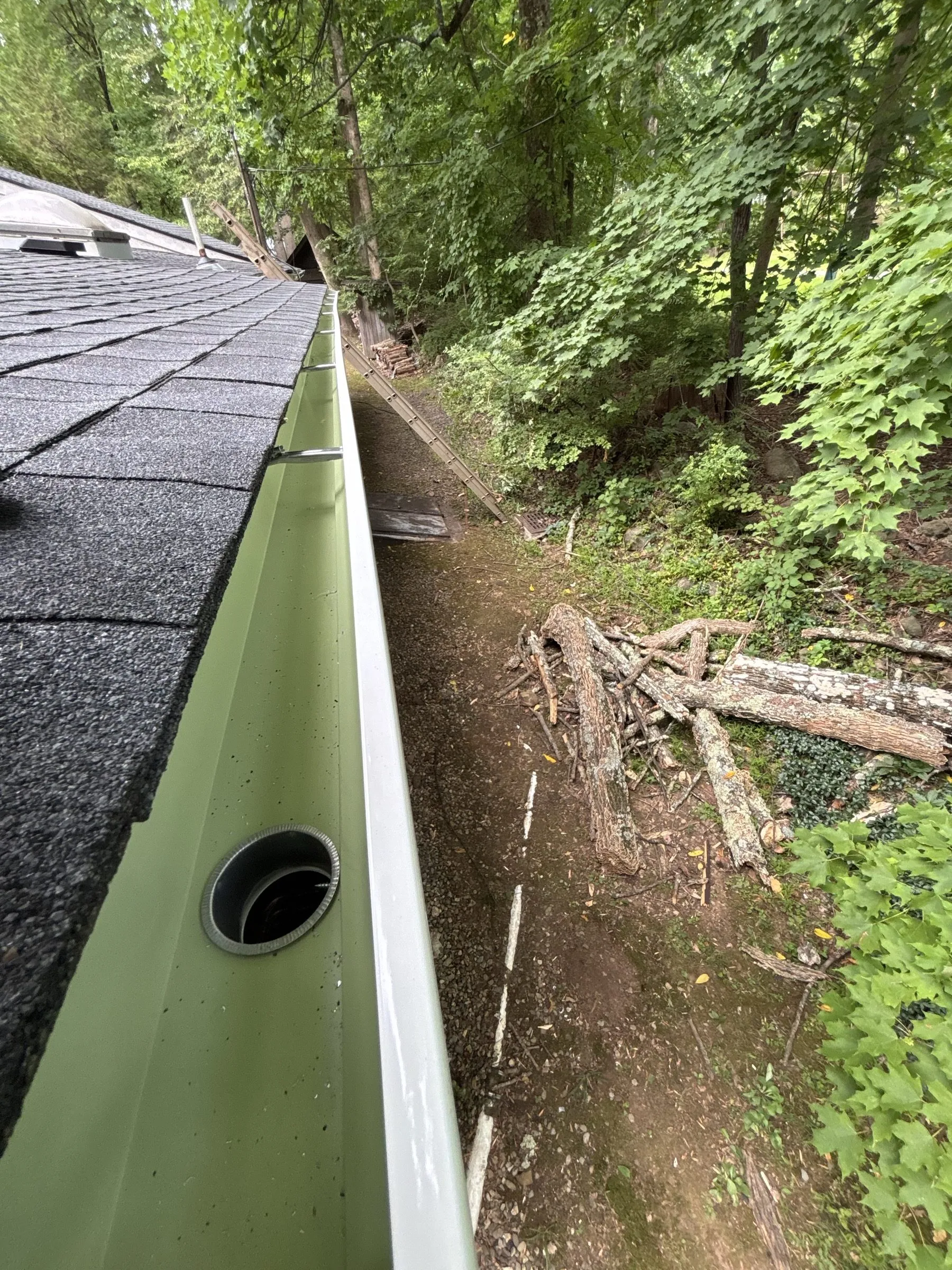 The new gutter running along the eave below the finished shingles, outlet set in.