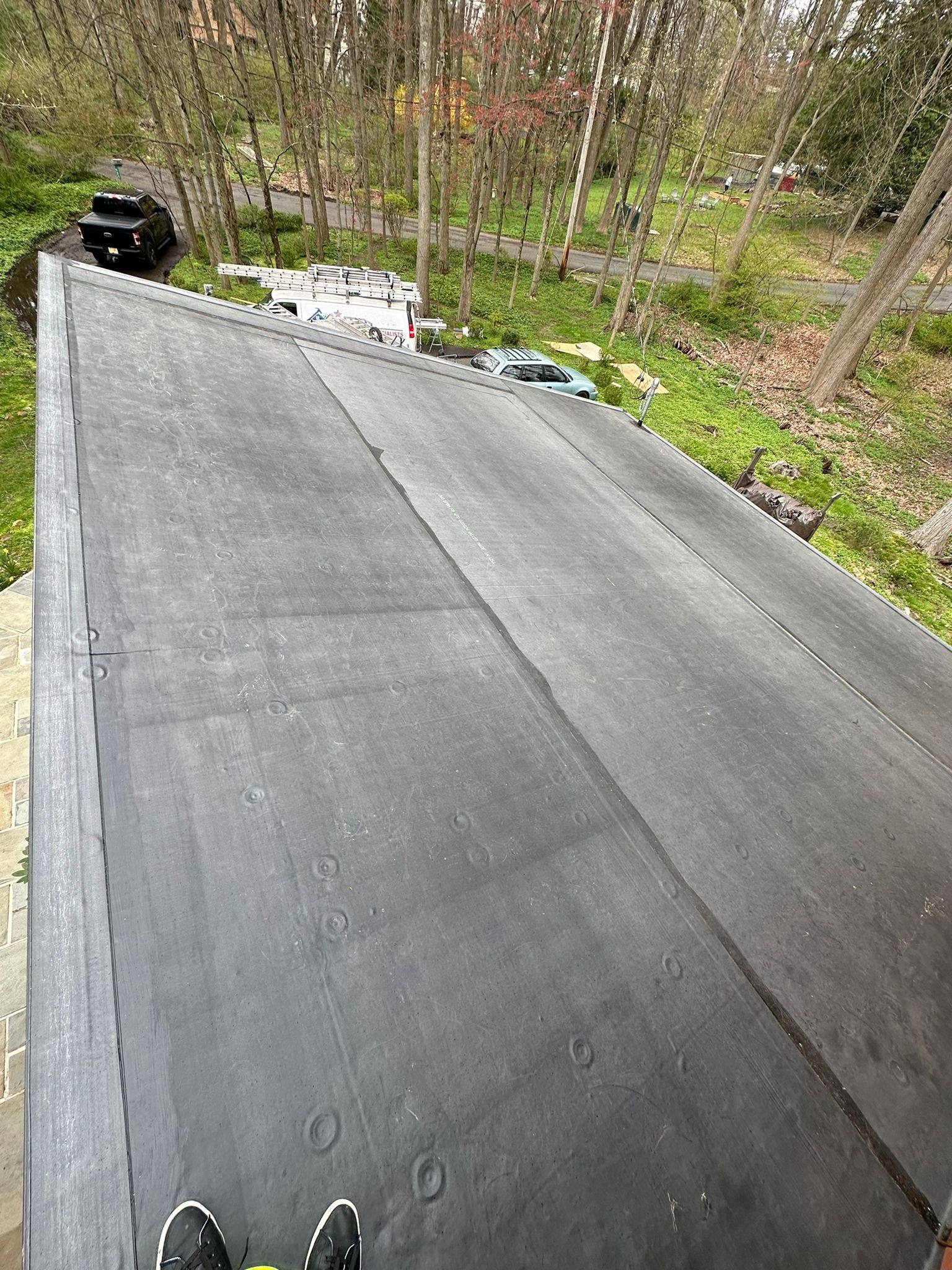 Finished EPDM flat roof in Berkeley Heights, the new black membrane running down the slope past the driveway.