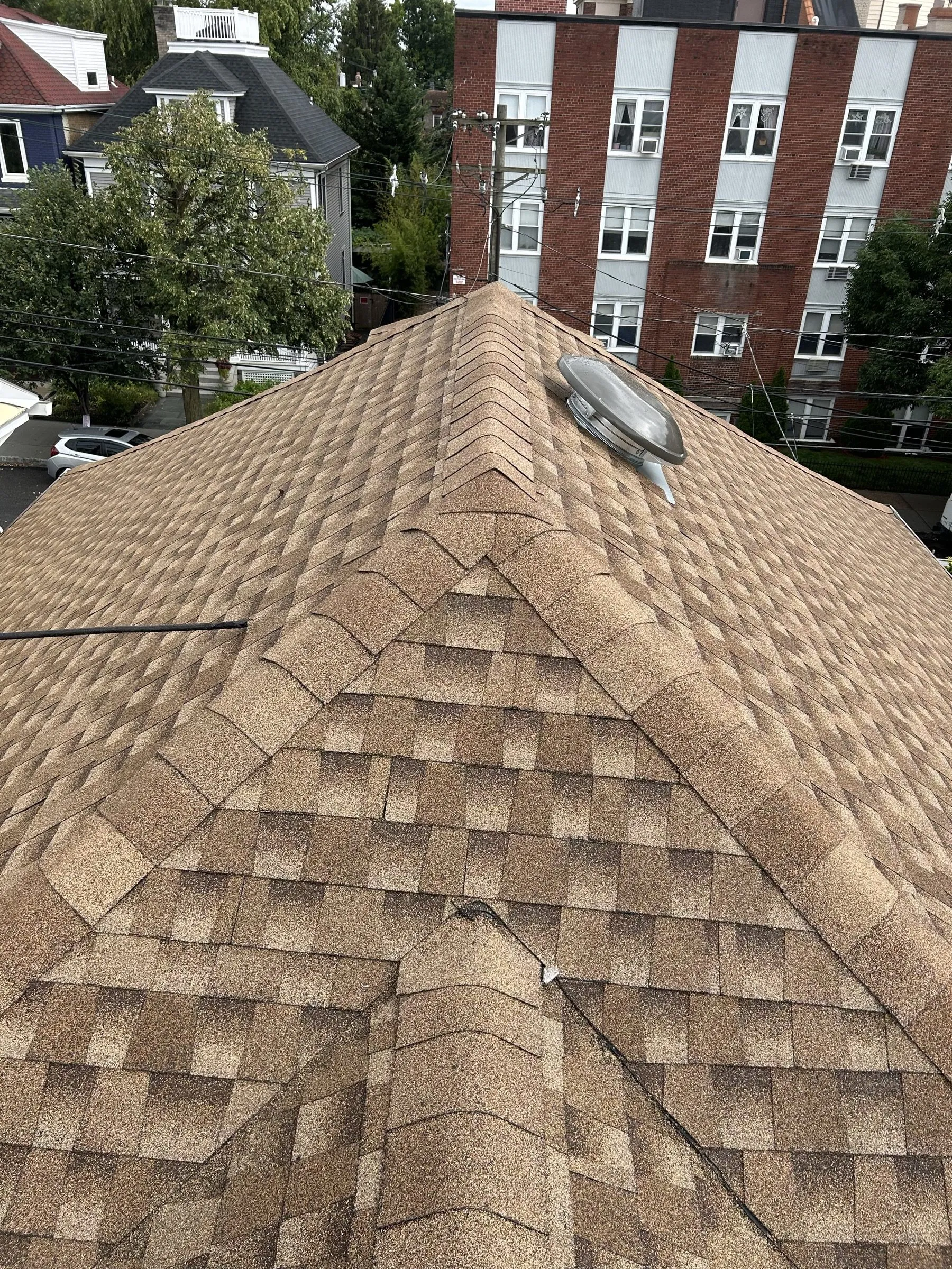 New shingles across the finished roof, neighboring rooftops falling away below.