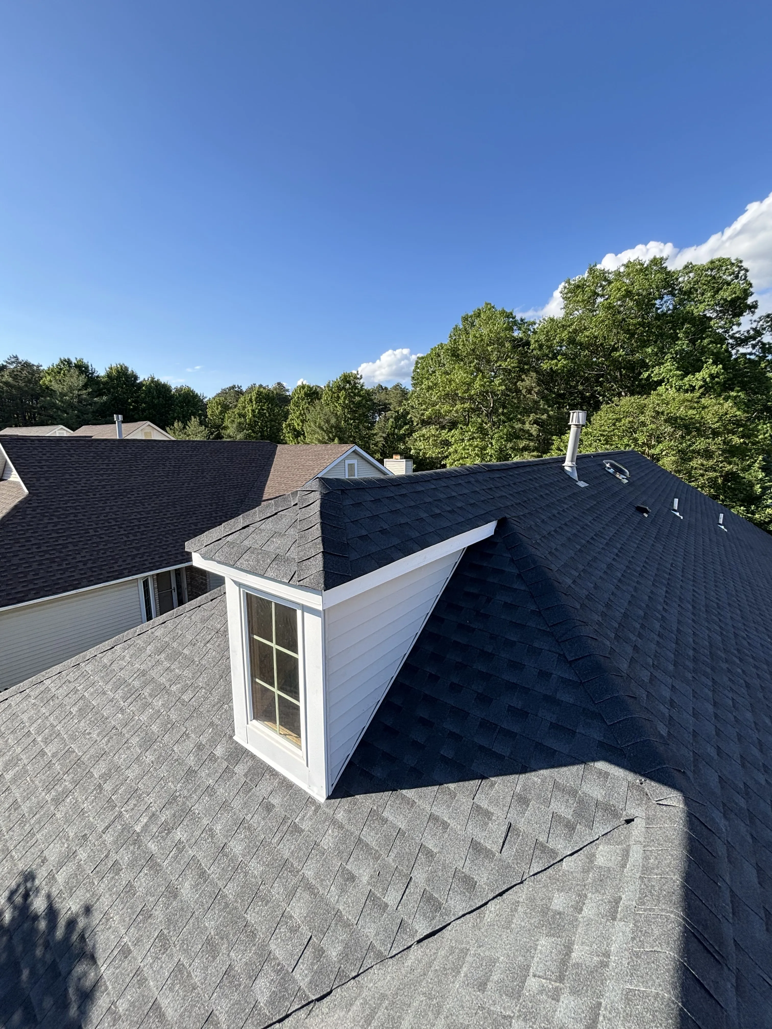 Finished shingle roof with a dormer and new metal valley, crisp lines against a clear sky.