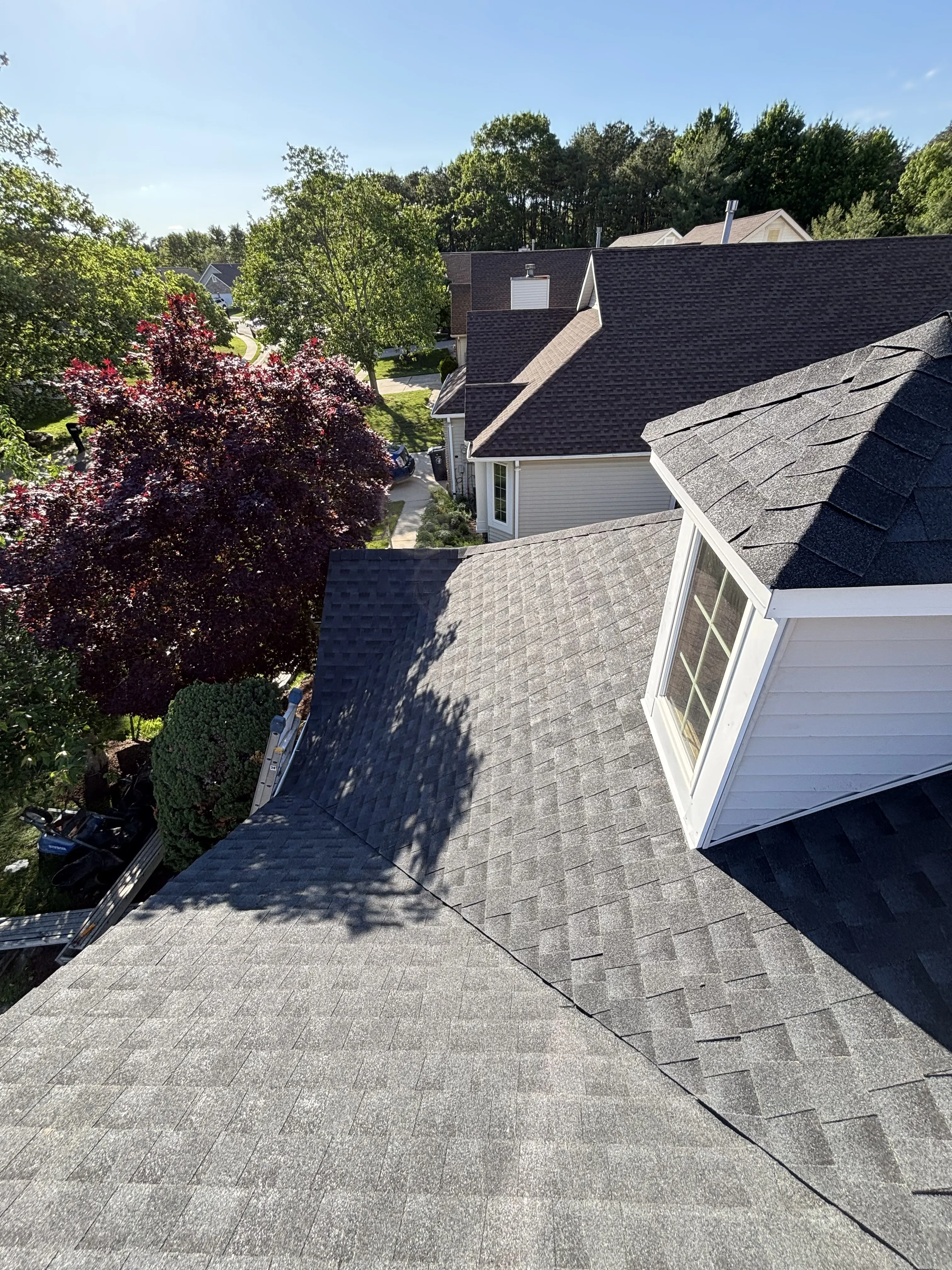 Completed shingle roof wrapping a dormer, viewed over the front landscaping of the home.