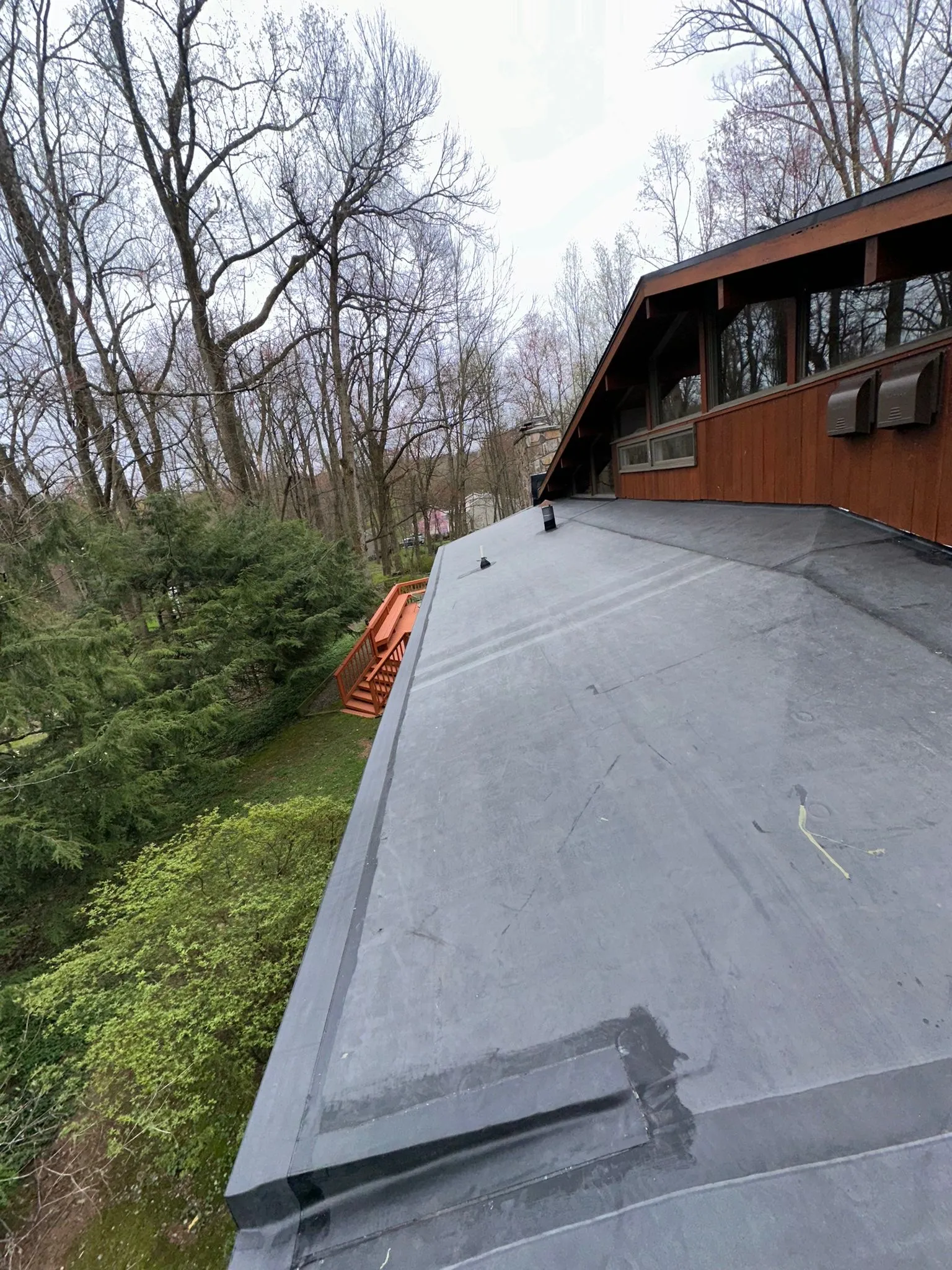 Completed EPDM roof and edging running along the cedar-sided home above the wooded back deck.