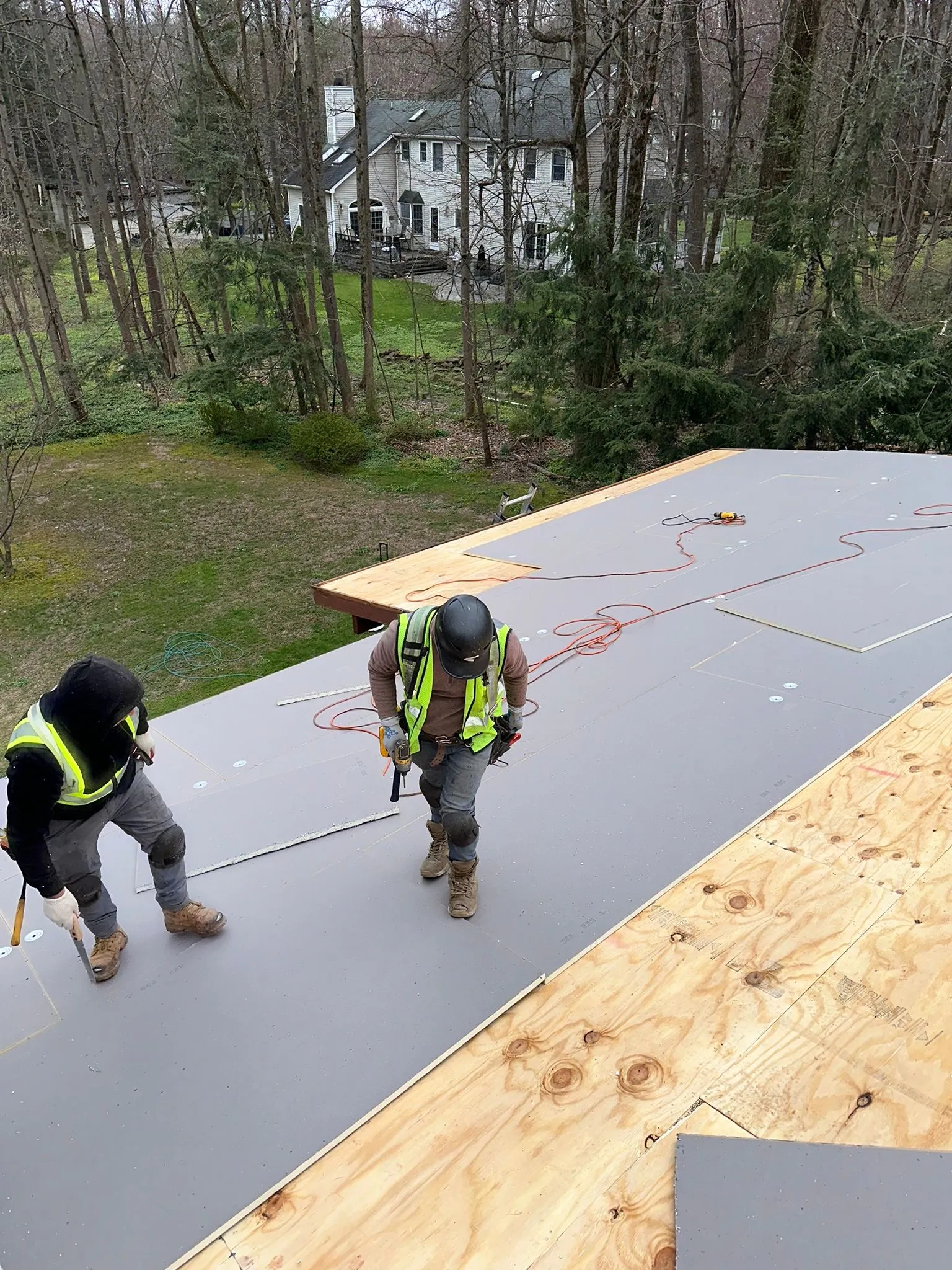 Crew fastening gray insulation board over the new decking, half boarded and half bare plywood.