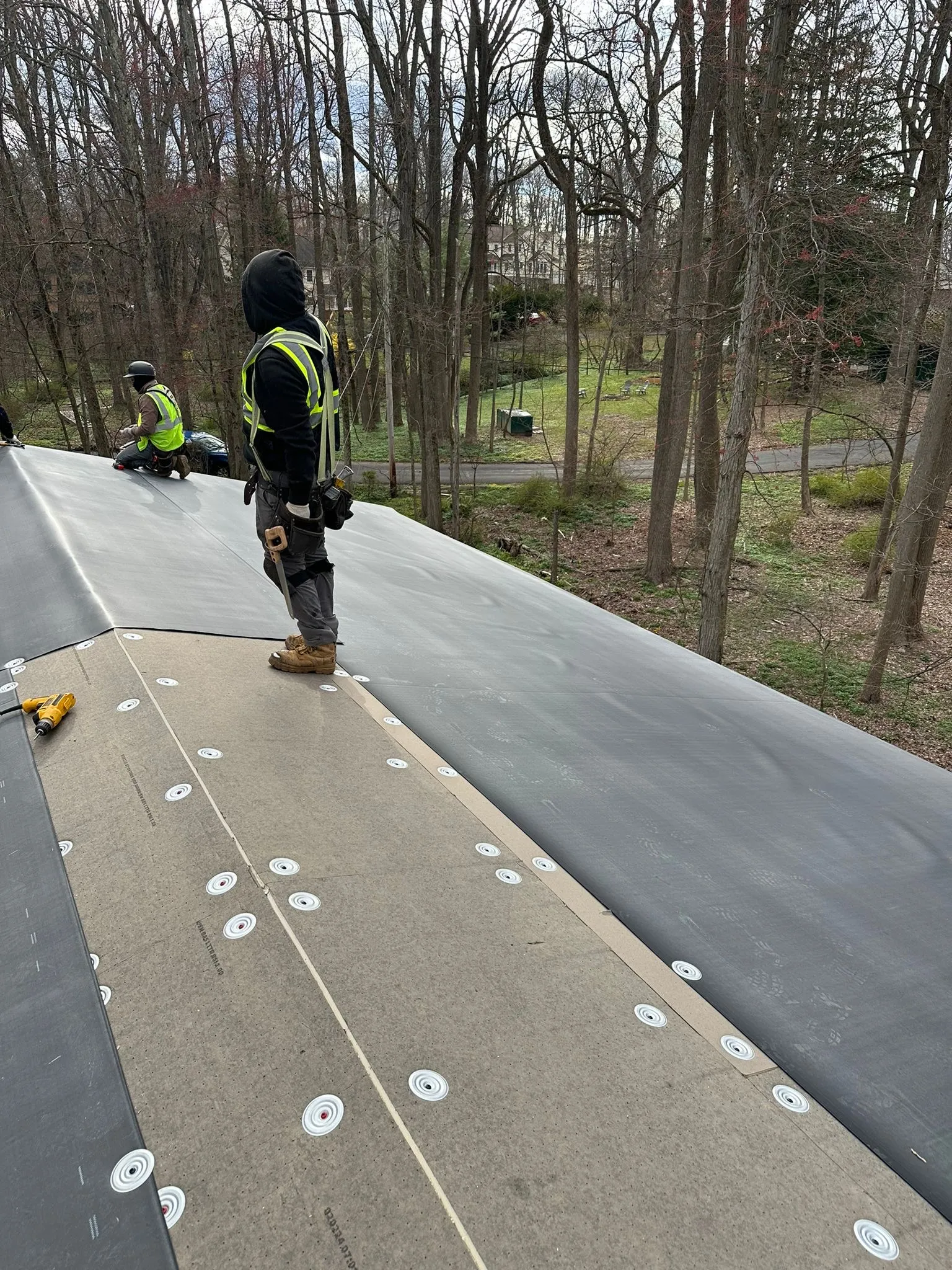 EPDM membrane unrolled over the fastener-plated insulation, a roofer at the new sheet's edge.