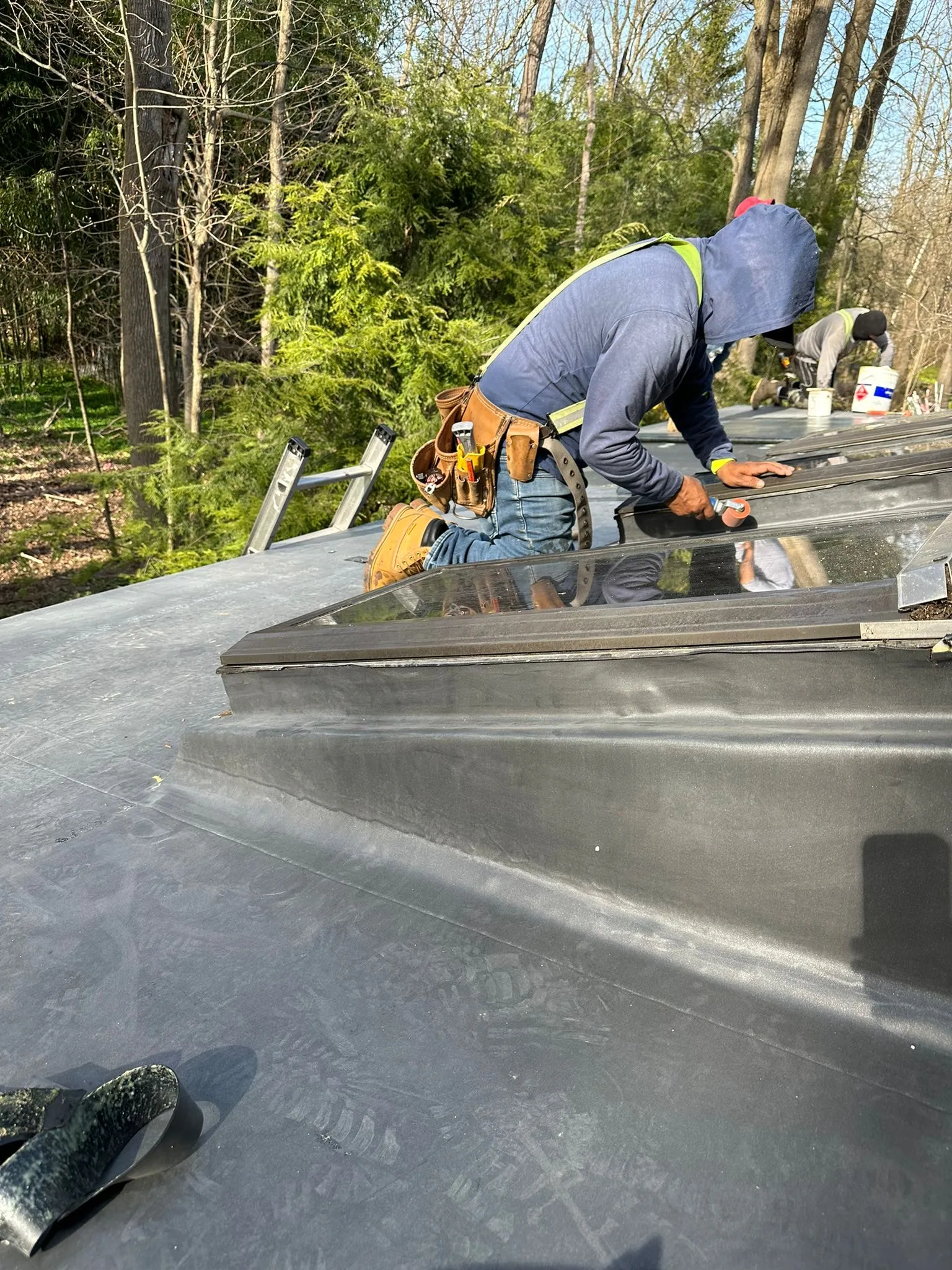 Roofer bonding EPDM membrane and flashing around a skylight curb on the new flat roof.