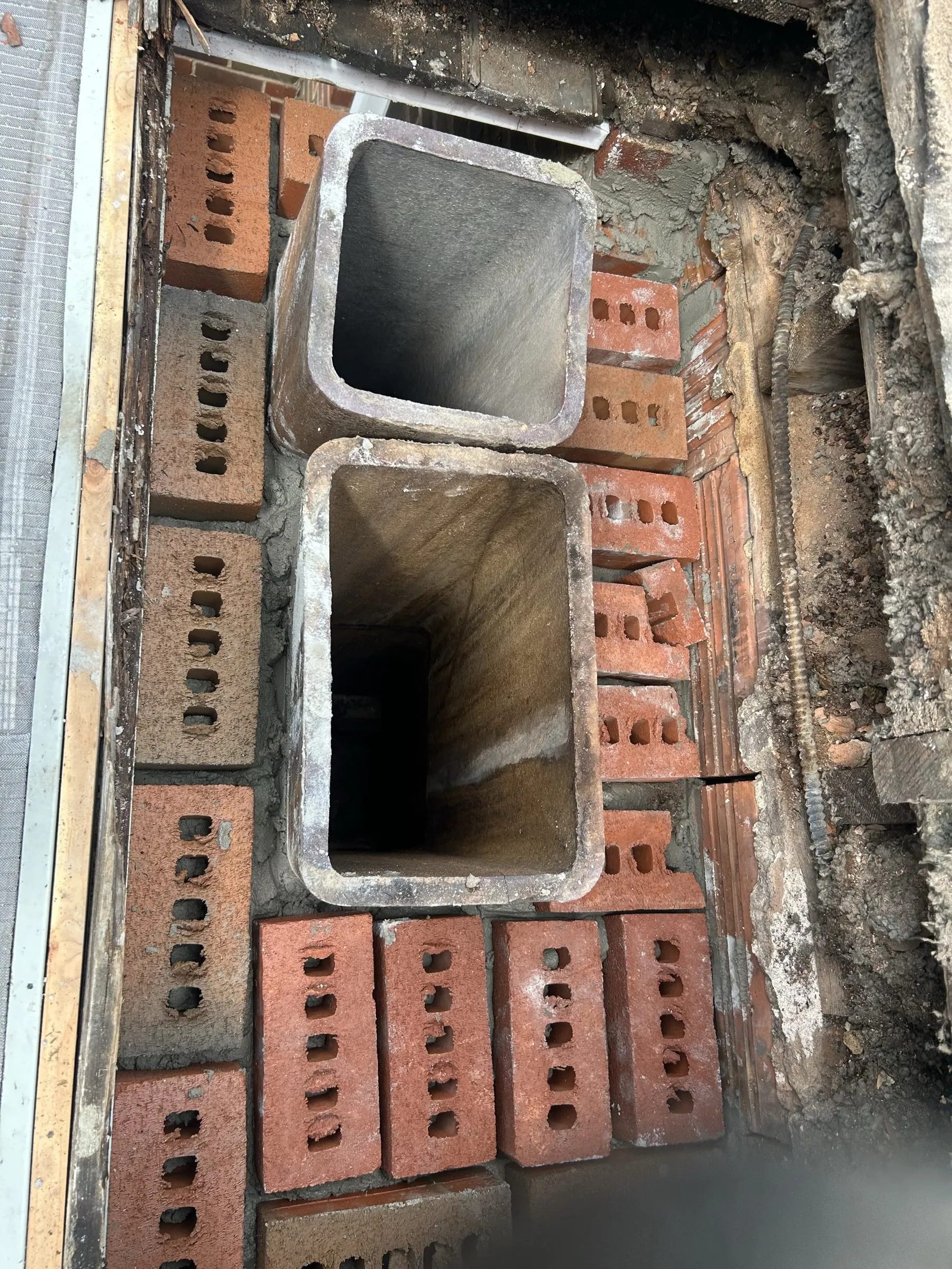 New clay flue liners set into the rebuilt brick base, fresh bricks stacked ready alongside.