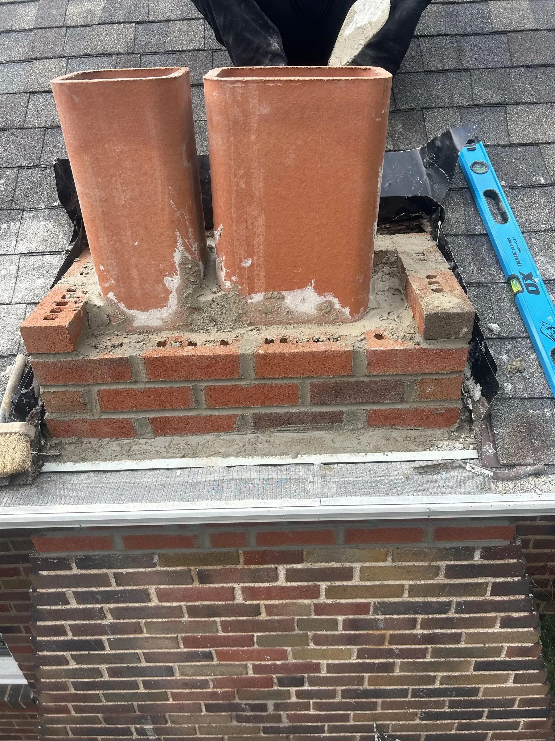 Two new flue liners standing in freshly laid brick courses, a level propped against the stack.