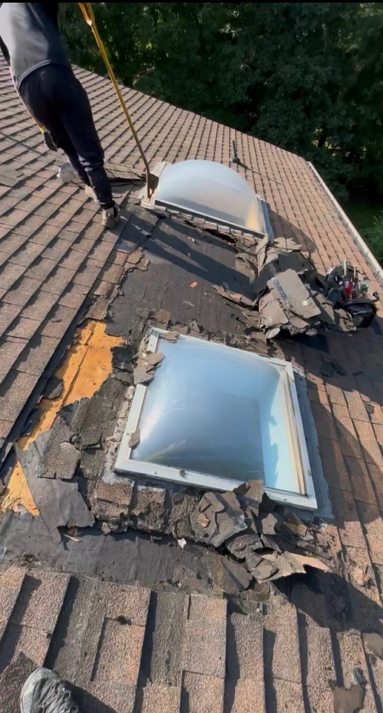 An old skylight opened up mid-replacement, torn shingles and debris cleared around the curb.