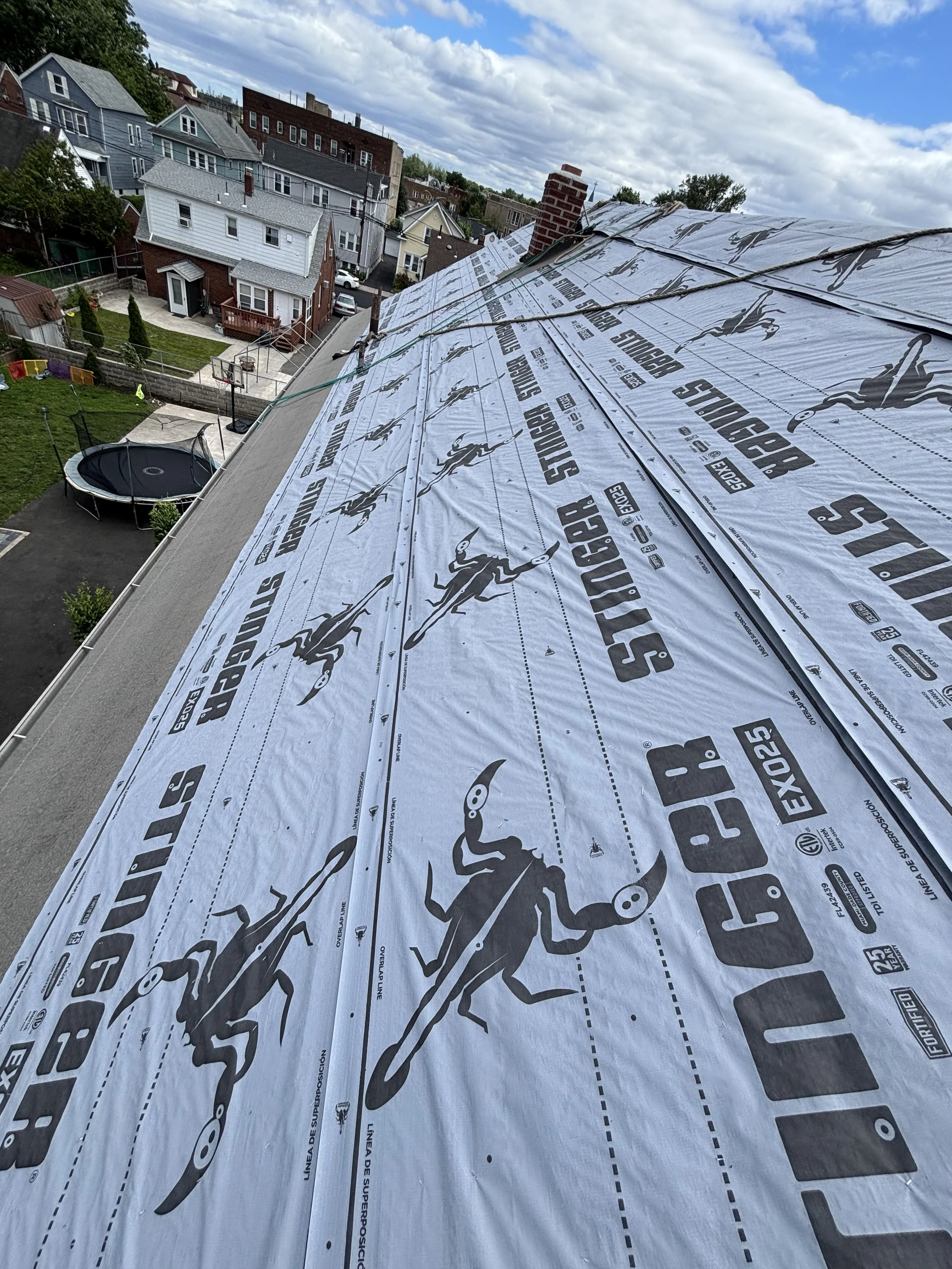 Synthetic underlayment rolled out and fastened across the new decking, weatherproofing the roof before shingles go on.