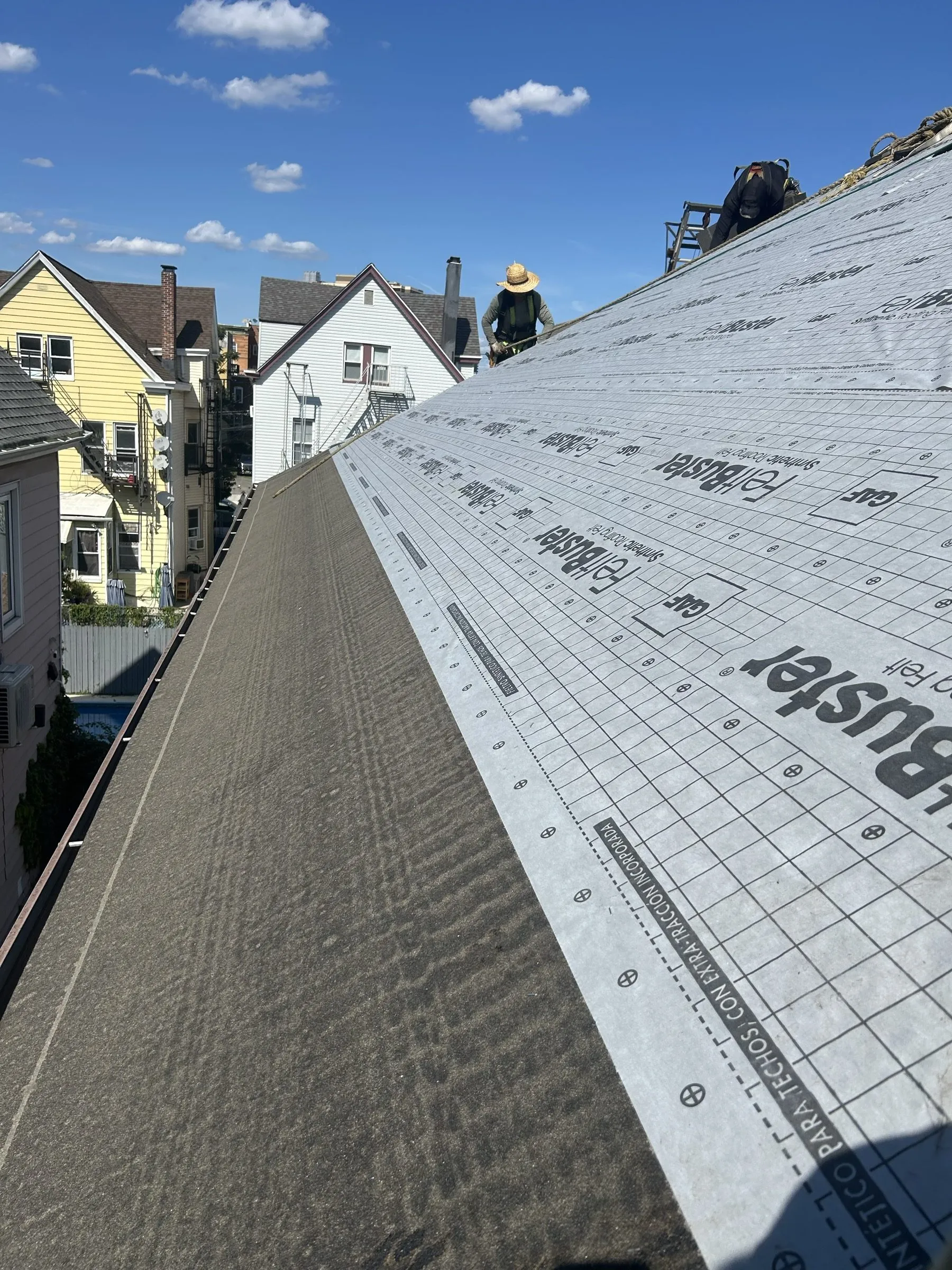Synthetic underlayment rolled out across the steep slope against open sky.