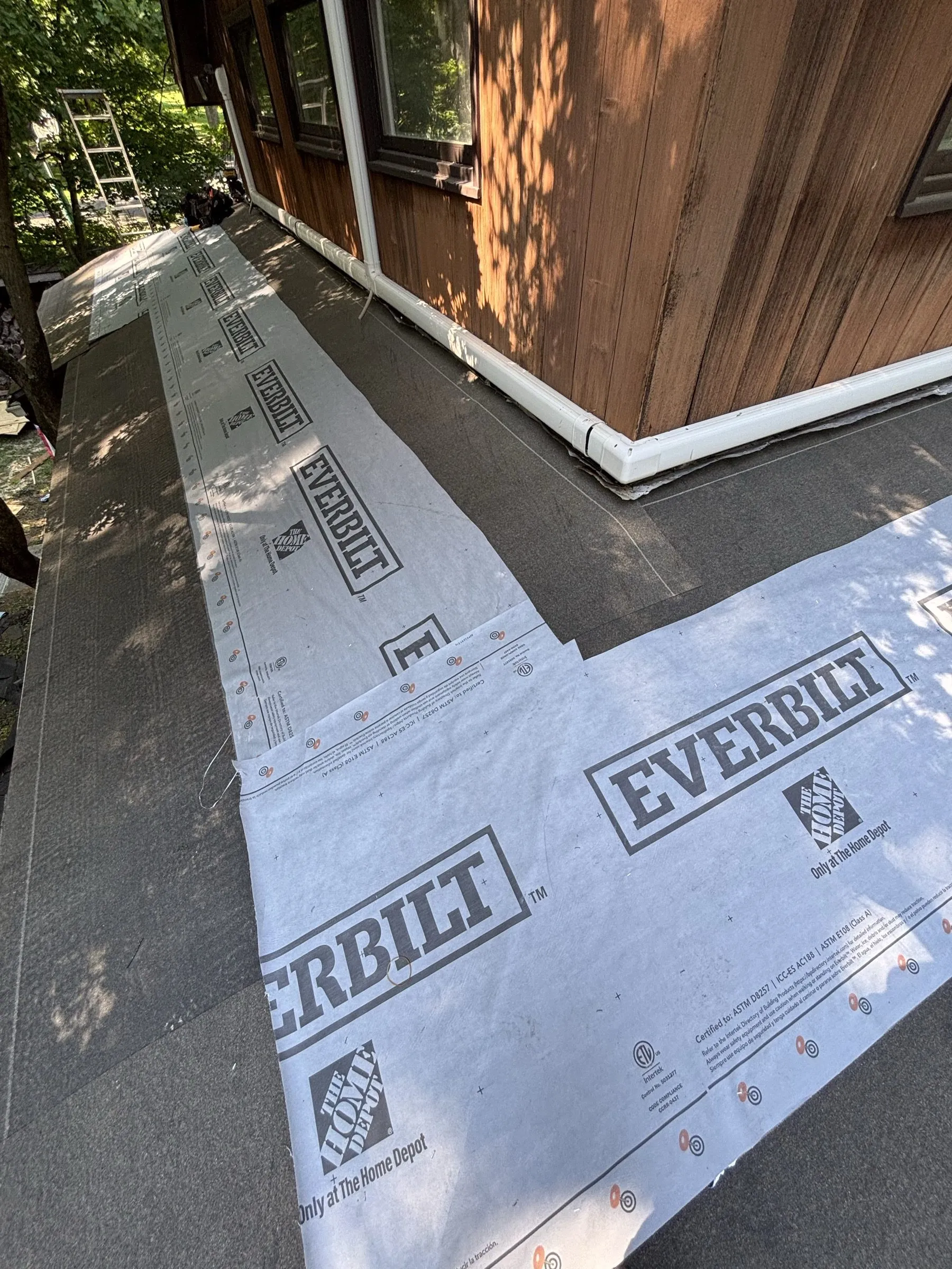 Synthetic underlayment meeting the drip edge, a section of new plywood still open above.